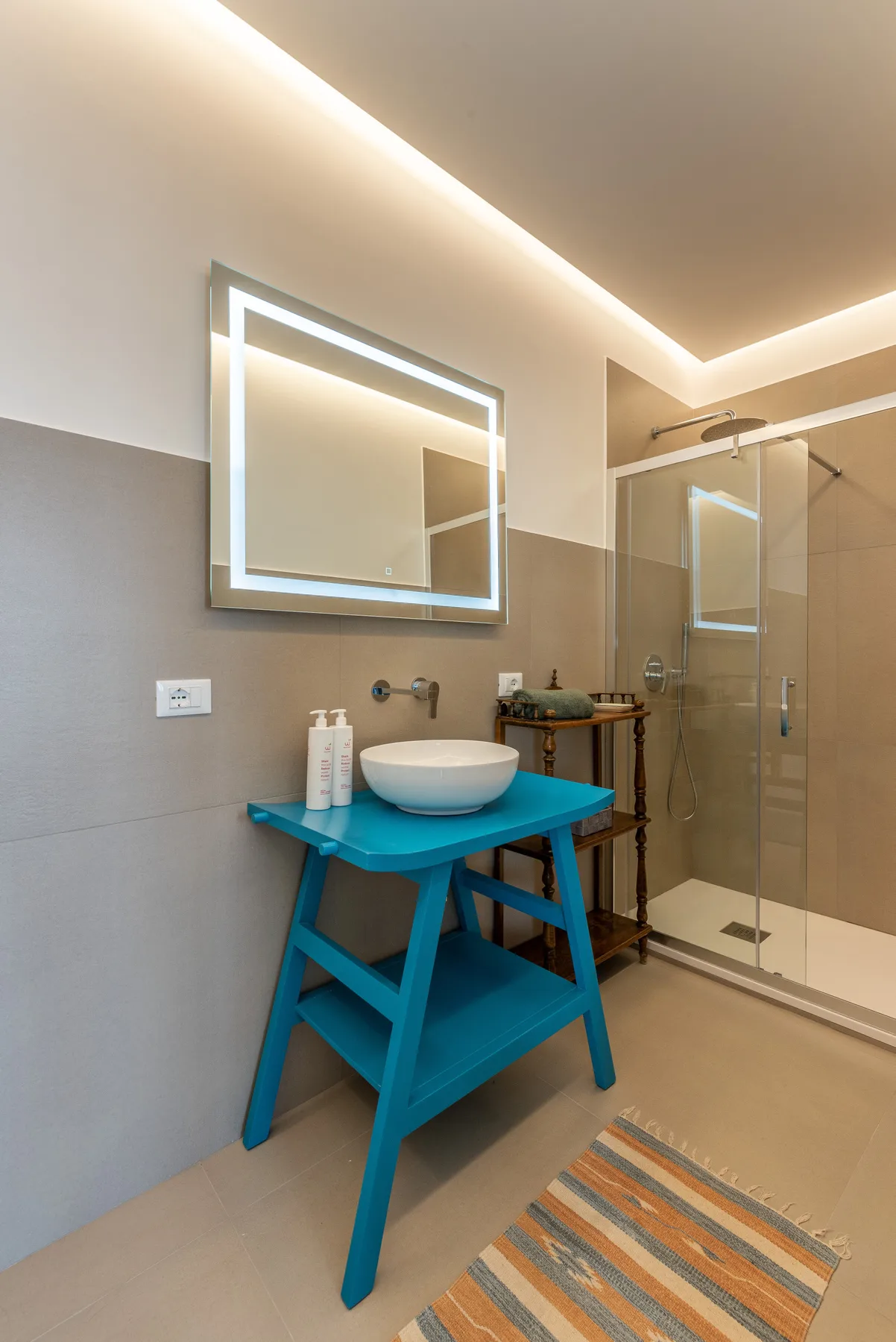 A modern bathroom with a turquoise washstand, illuminated mirror, and glass shower.