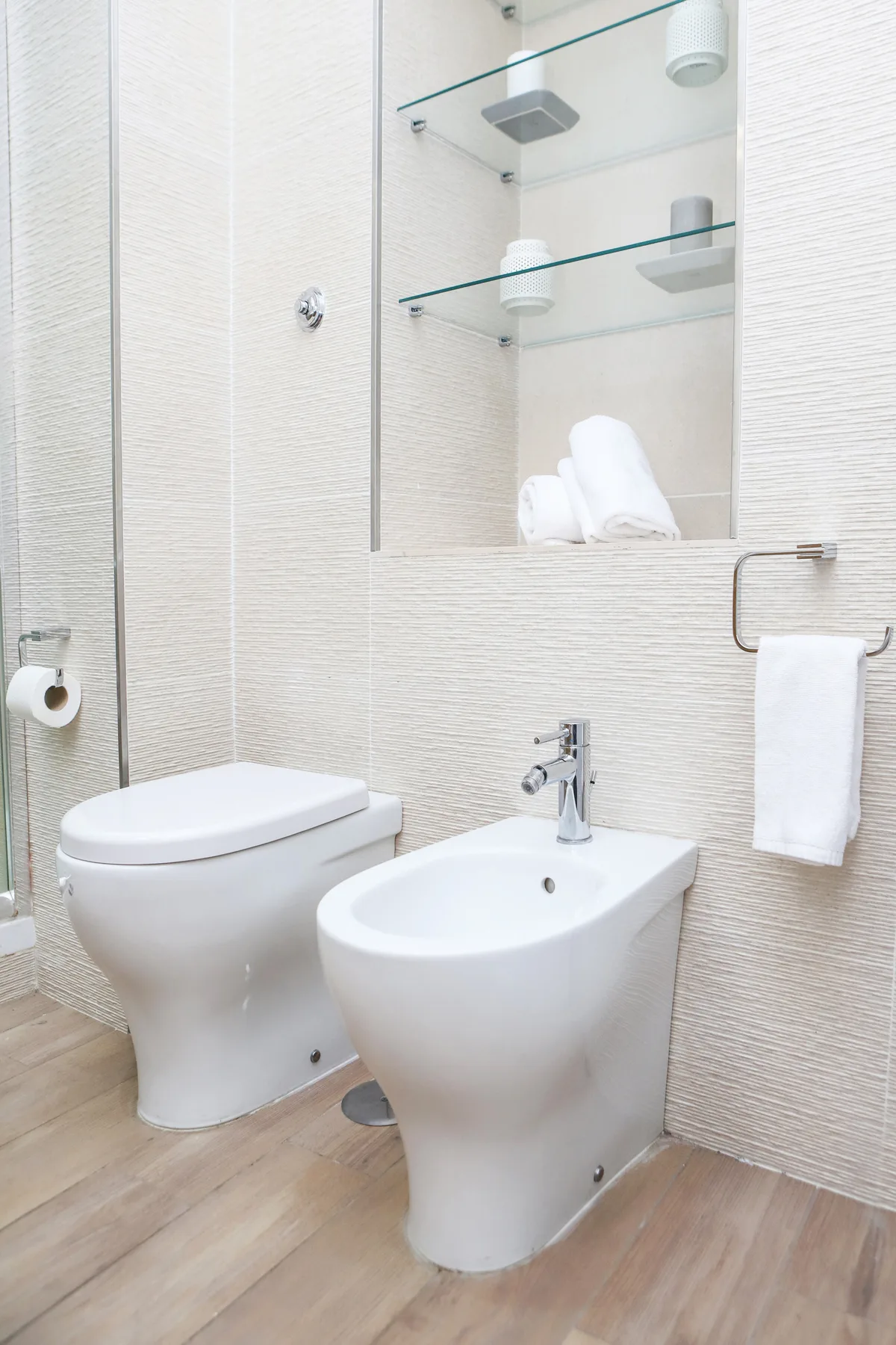 Un baño luminoso con inodoro, bidé y toalla colgada en la pared.