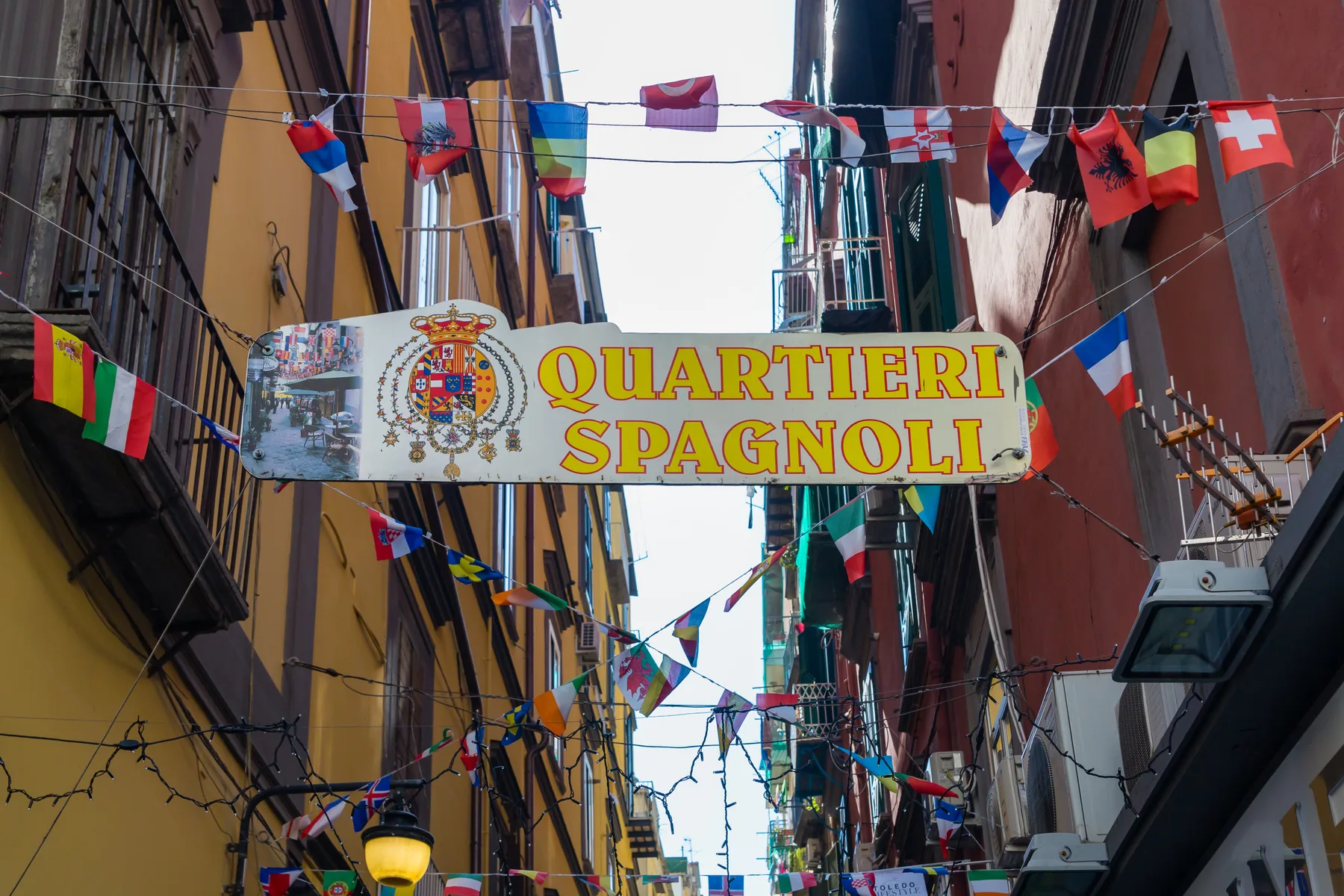 Una calle estrecha está decorada con banderas y un gran cartel del Quartiere Spagnolo.