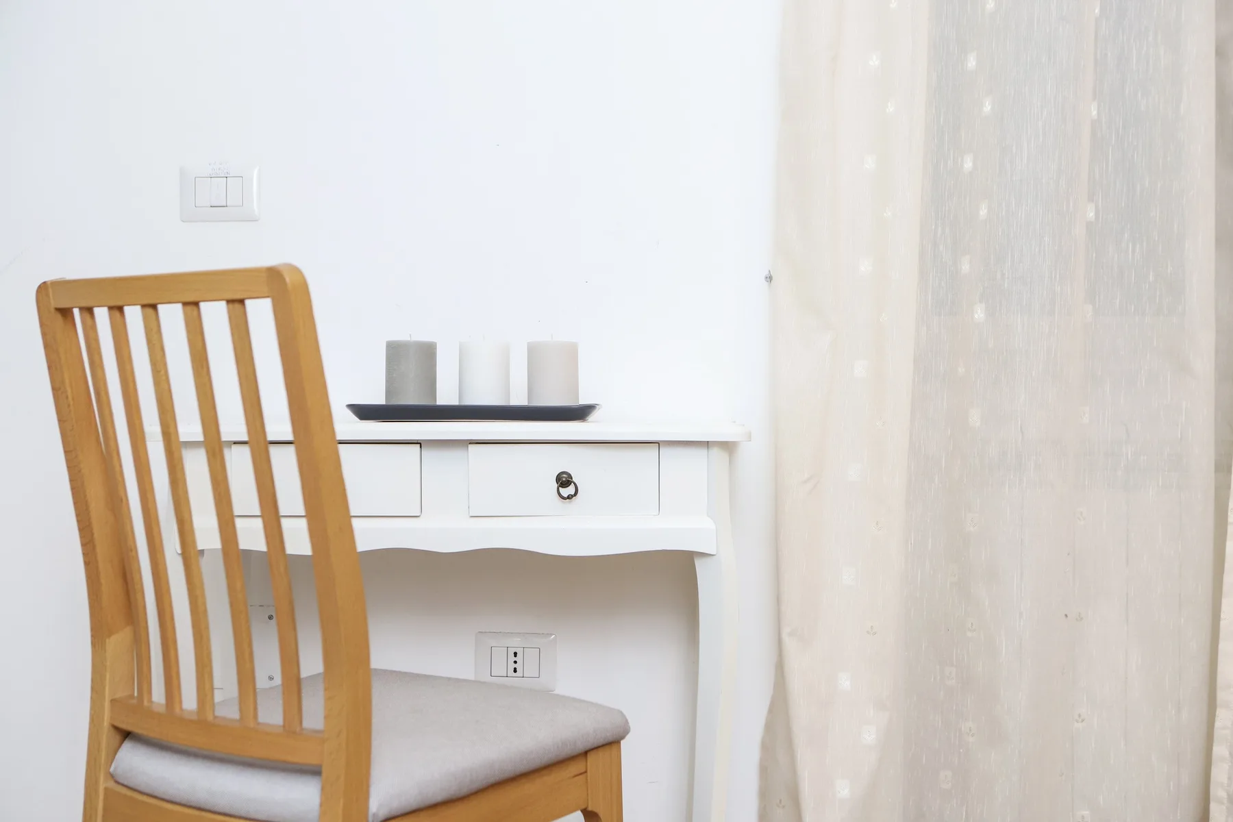 Un escritorio pequeño y un asiento de madera están junto a una cortina transparente.