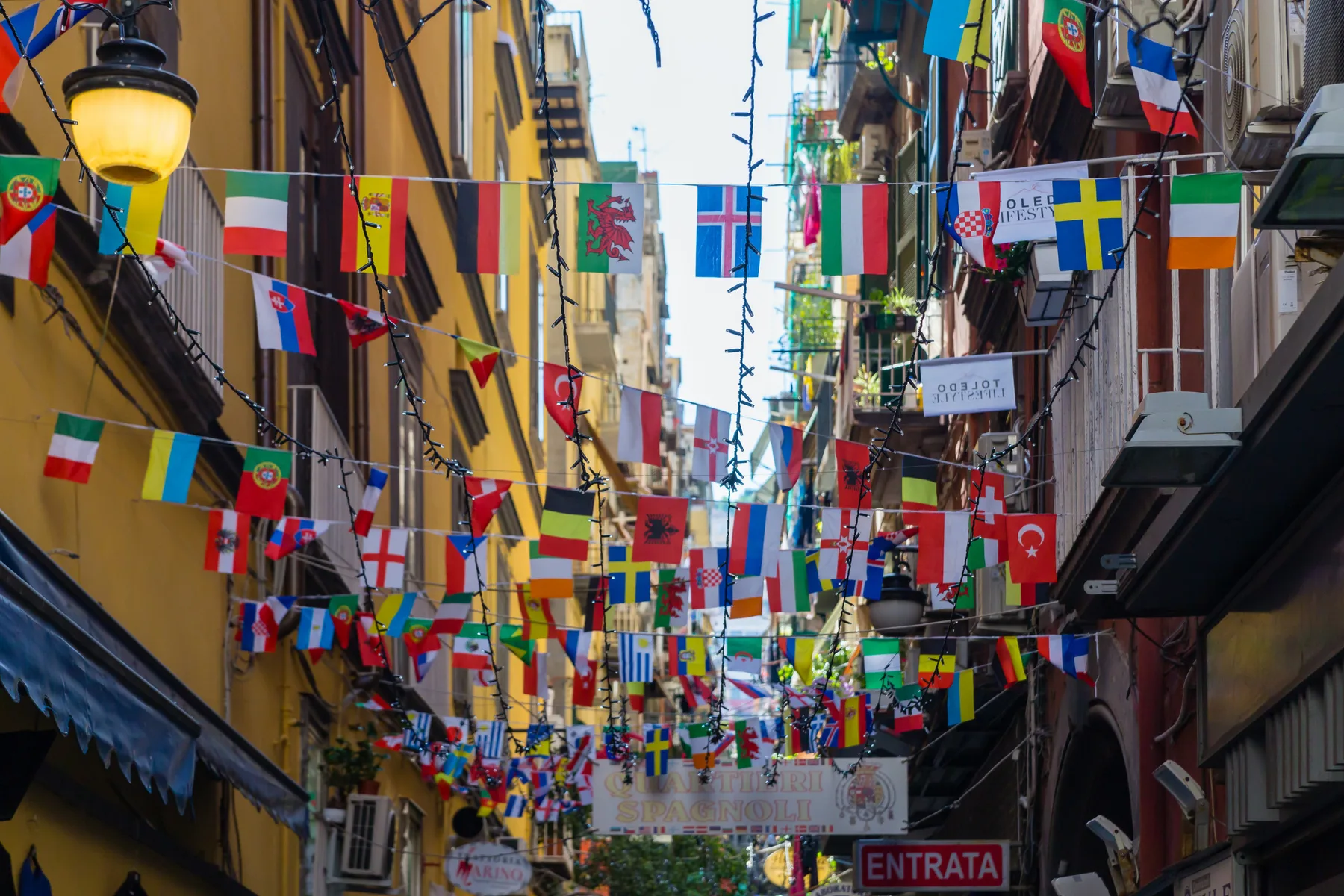 Una calle estrecha de la ciudad está flanqueada por edificios altos y banderas de colores.