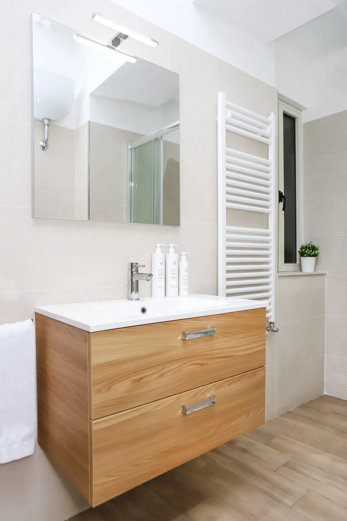 Un baño luminoso con mueble de madera, espejo de pared y radiador toallero.
