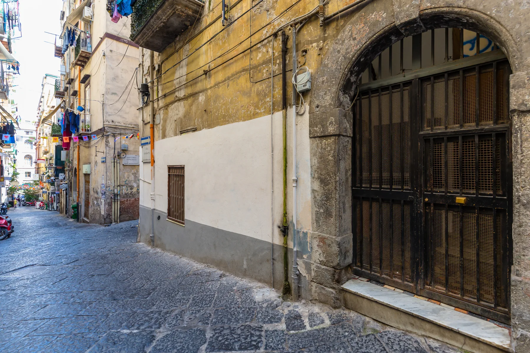 Una calle estrecha empedrada pasa junto a edificios antiguos y una gran entrada arqueada.