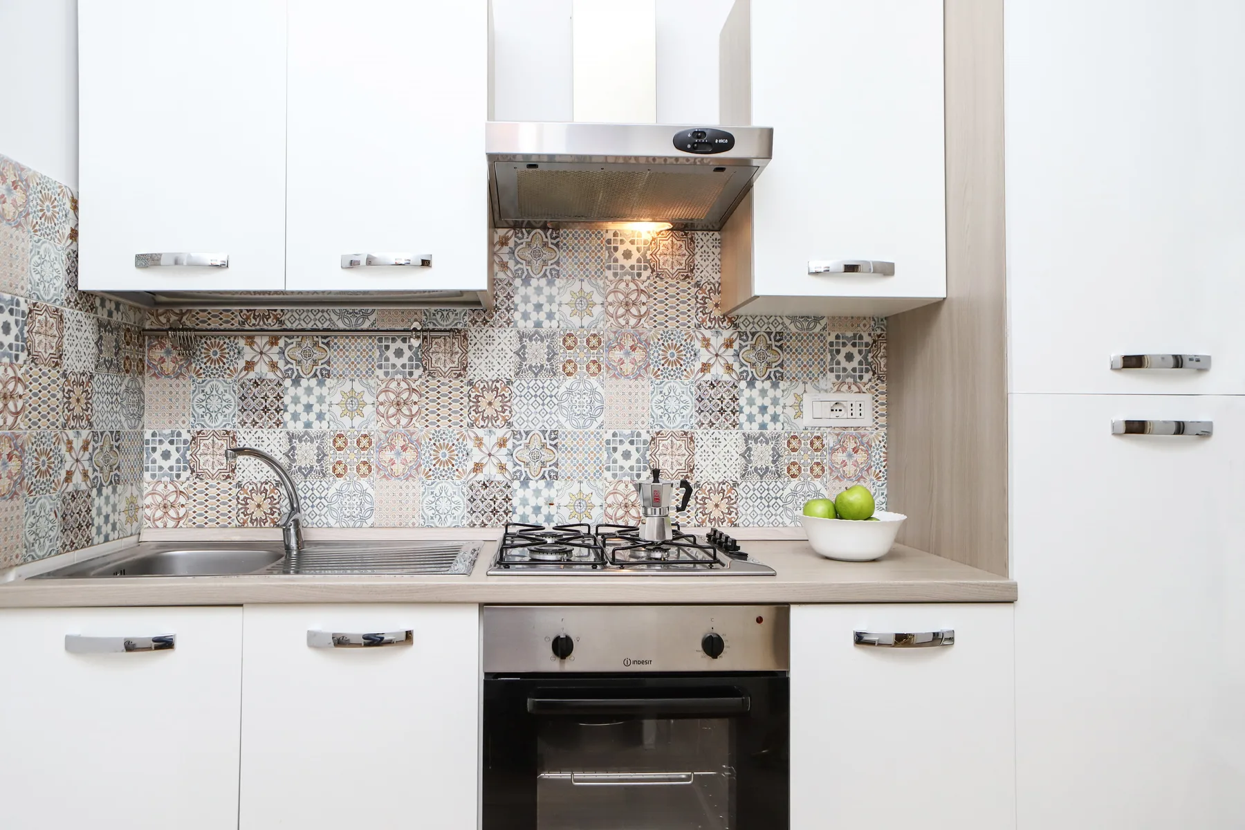 Una cocina luminosa con gabinetes blancos, un salpicadero estampado y una placa de cocina.