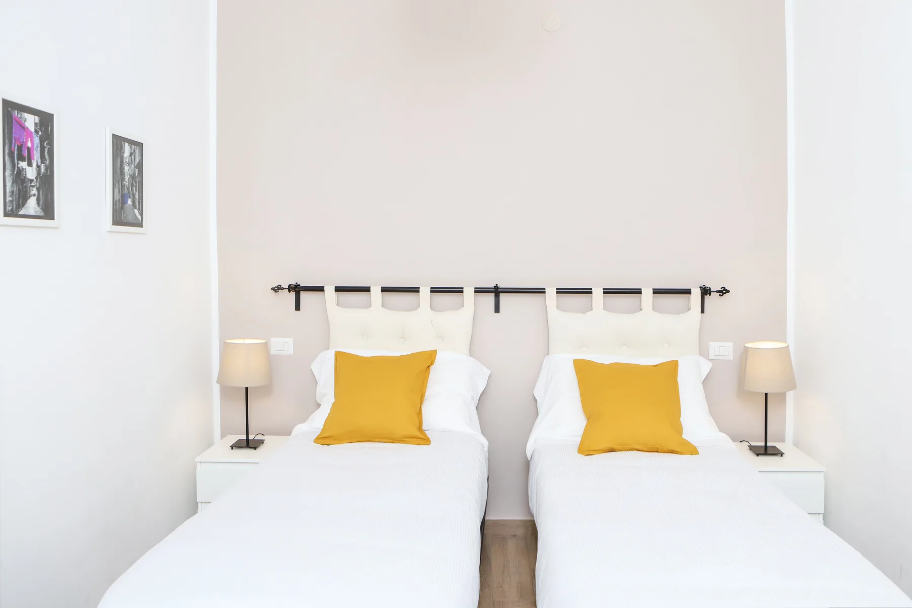 Un dormitorio luminoso con dos camas individuales, ropa de cama blanca y cojines amarillos.