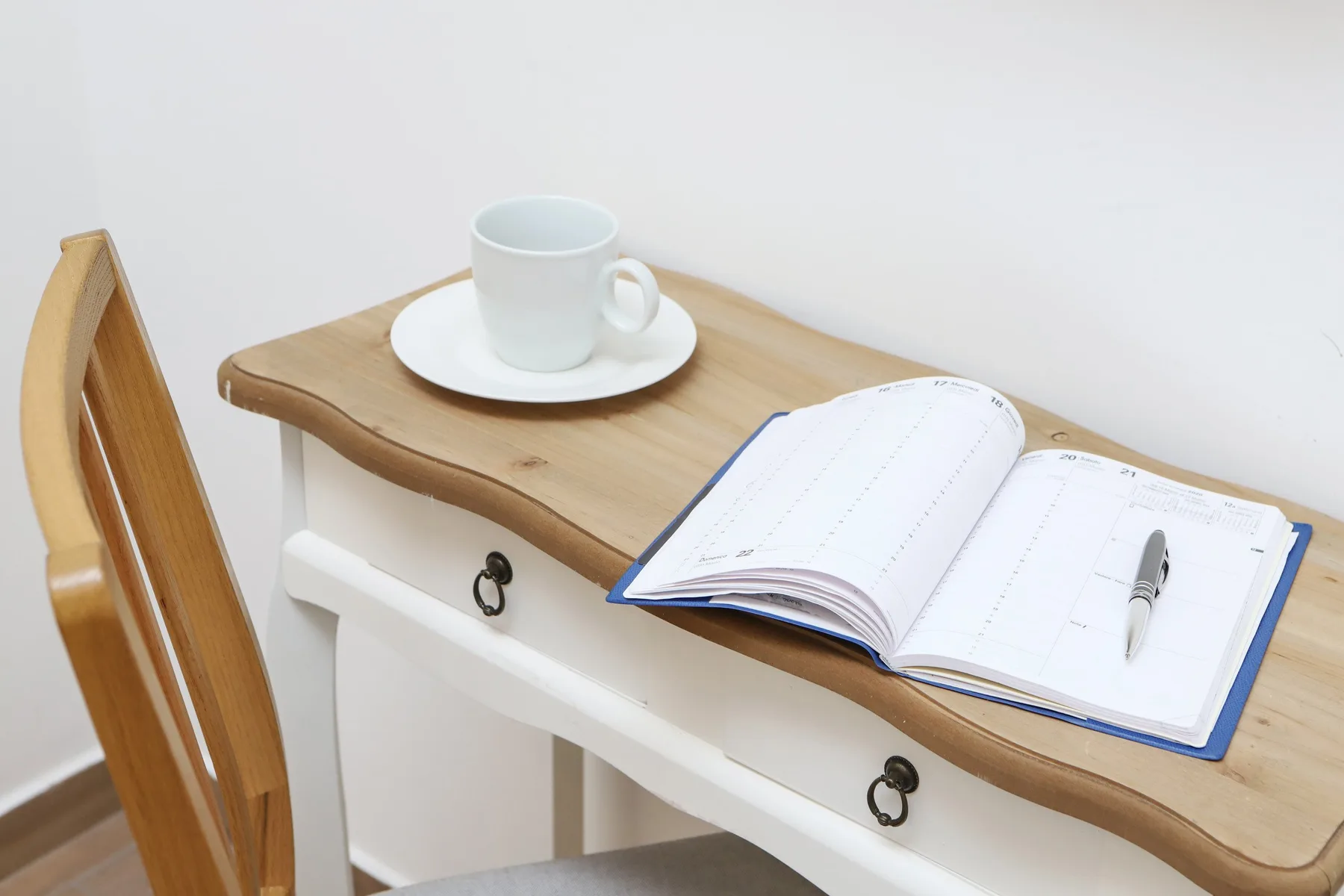 Un pequeño escritorio tiene una agenda abierta y una taza.