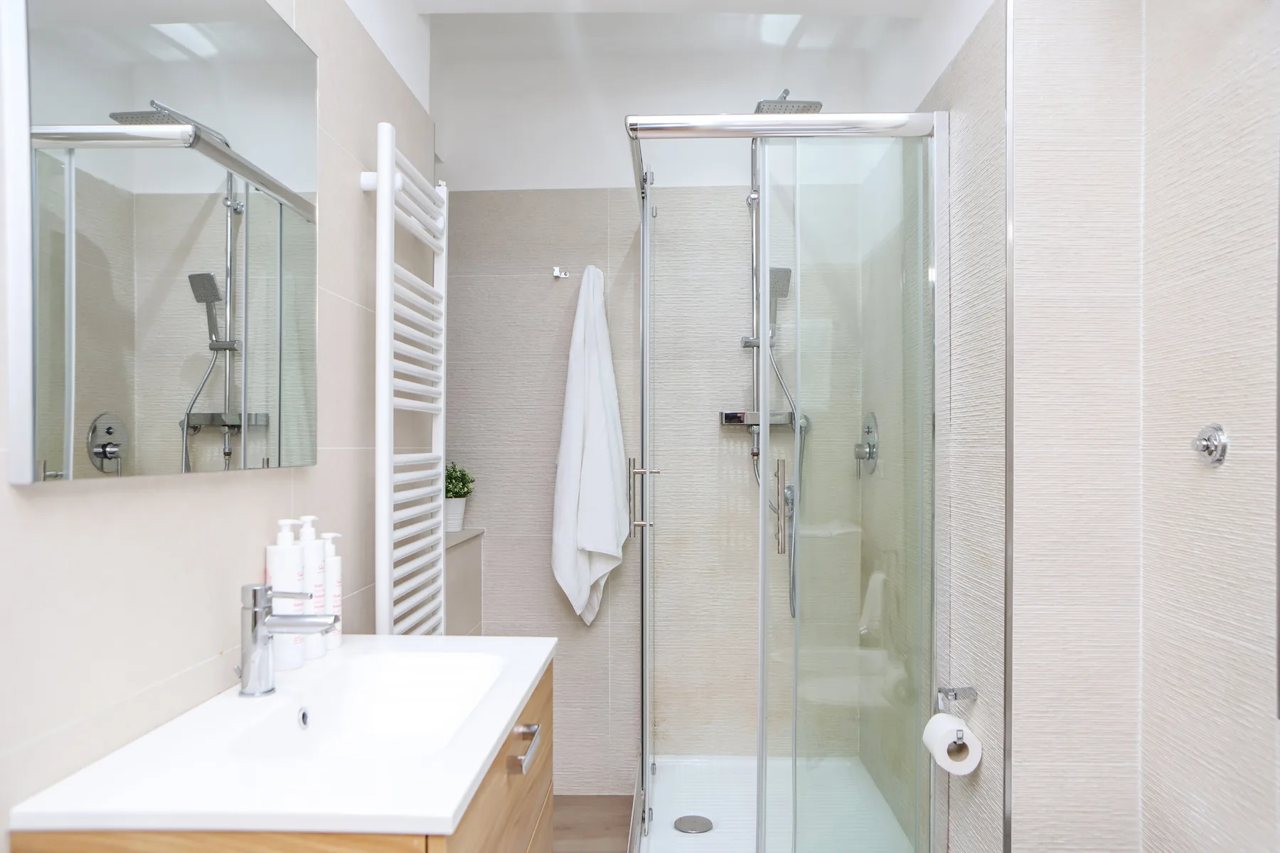 Un baño luminoso con lavabo, espejo y ducha de vidrio.