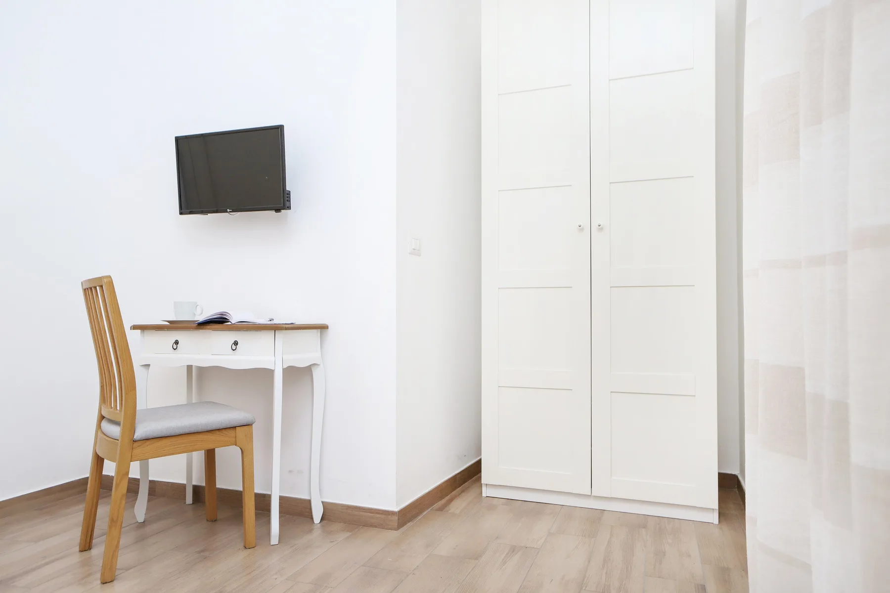 Una habitación luminosa con escritorio, silla, televisor en la pared y puertas de armario blancas.