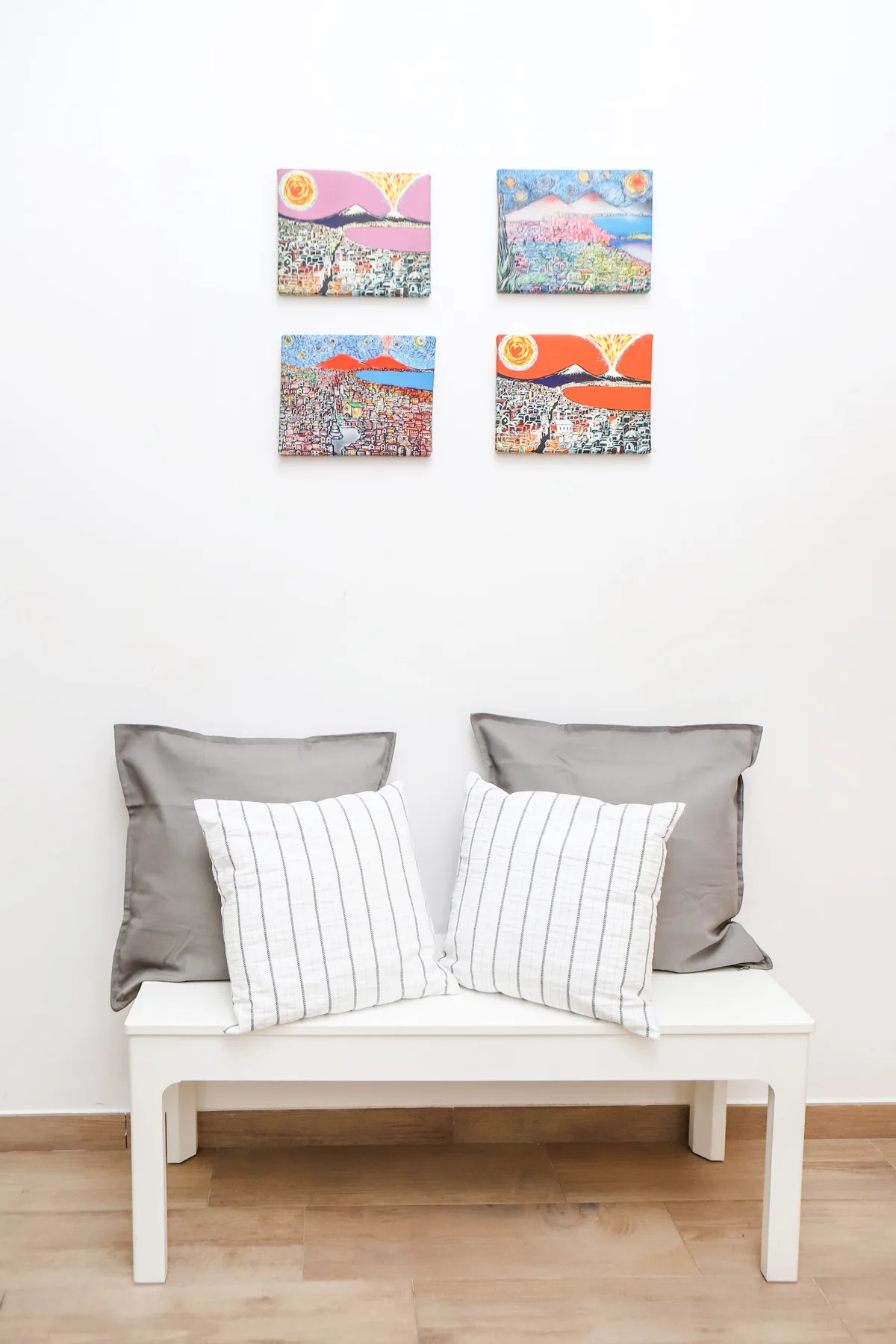 Un banco blanco con cojines está debajo de cuatro cuadros coloridos en una pared clara.