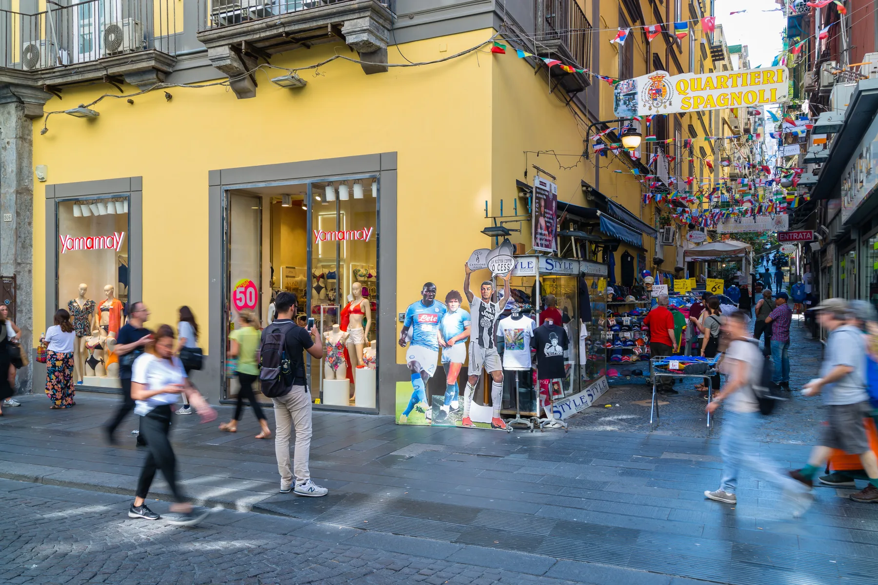 Una concurrida calle peatonal con tiendas y adornos coloridos colgantes.