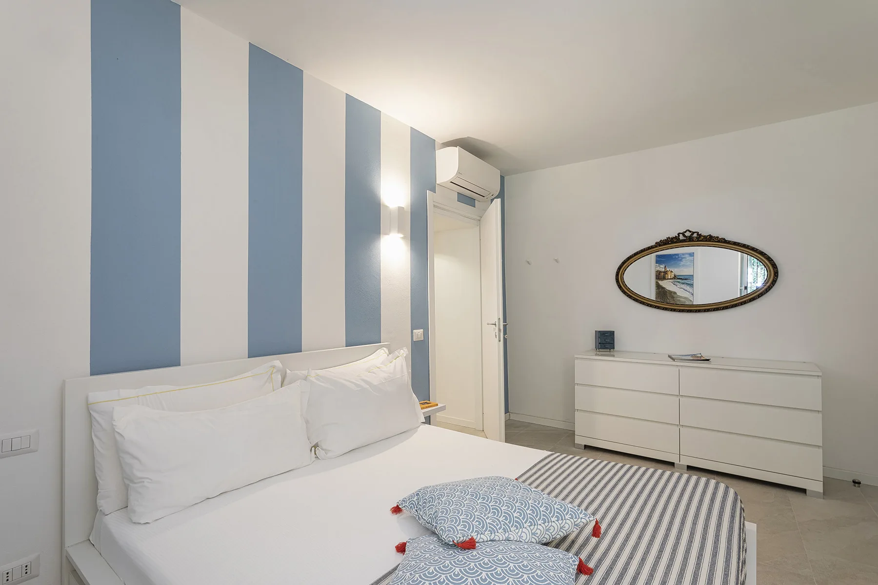 A bedroom with a bed, blue-and-white striped wall, and dresser.