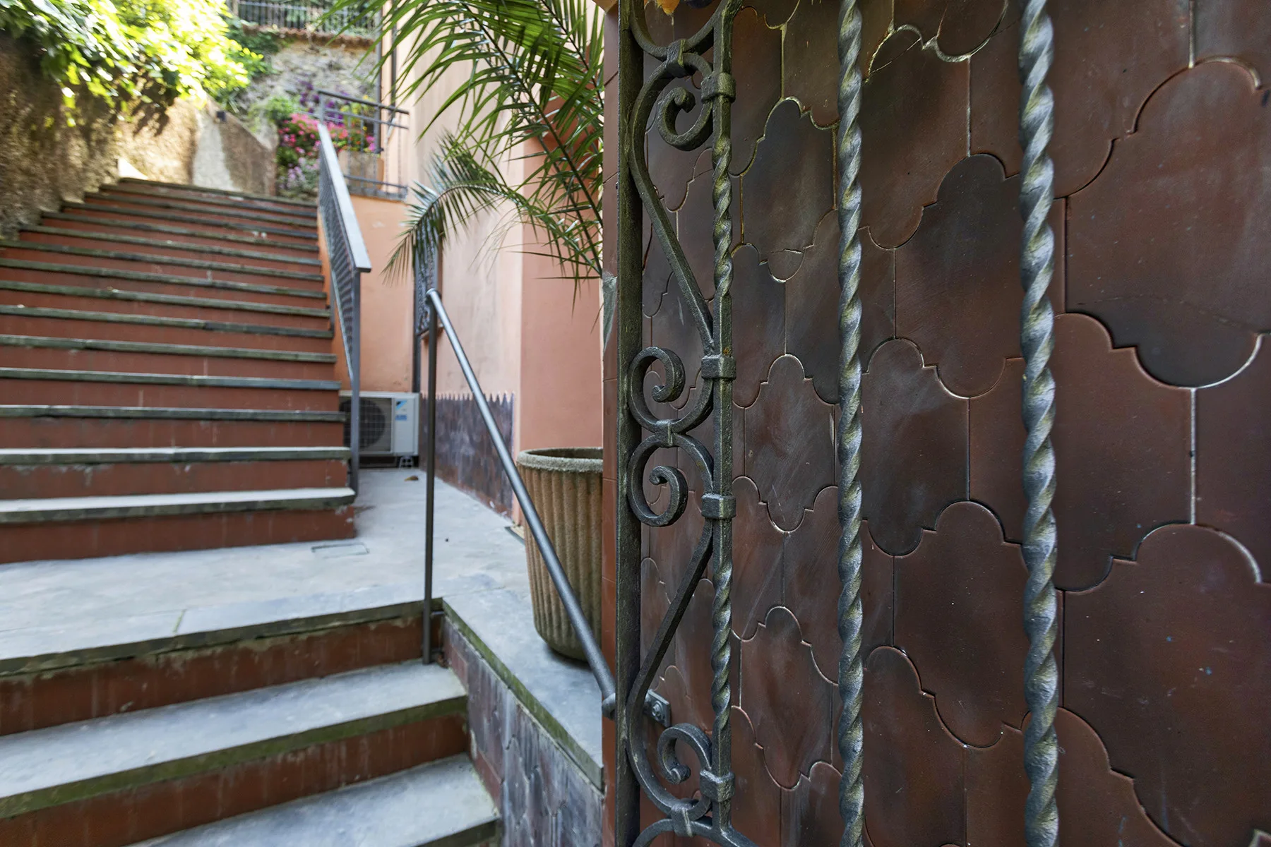 An outdoor stairway beside a decorative metal gate and leafy plants.