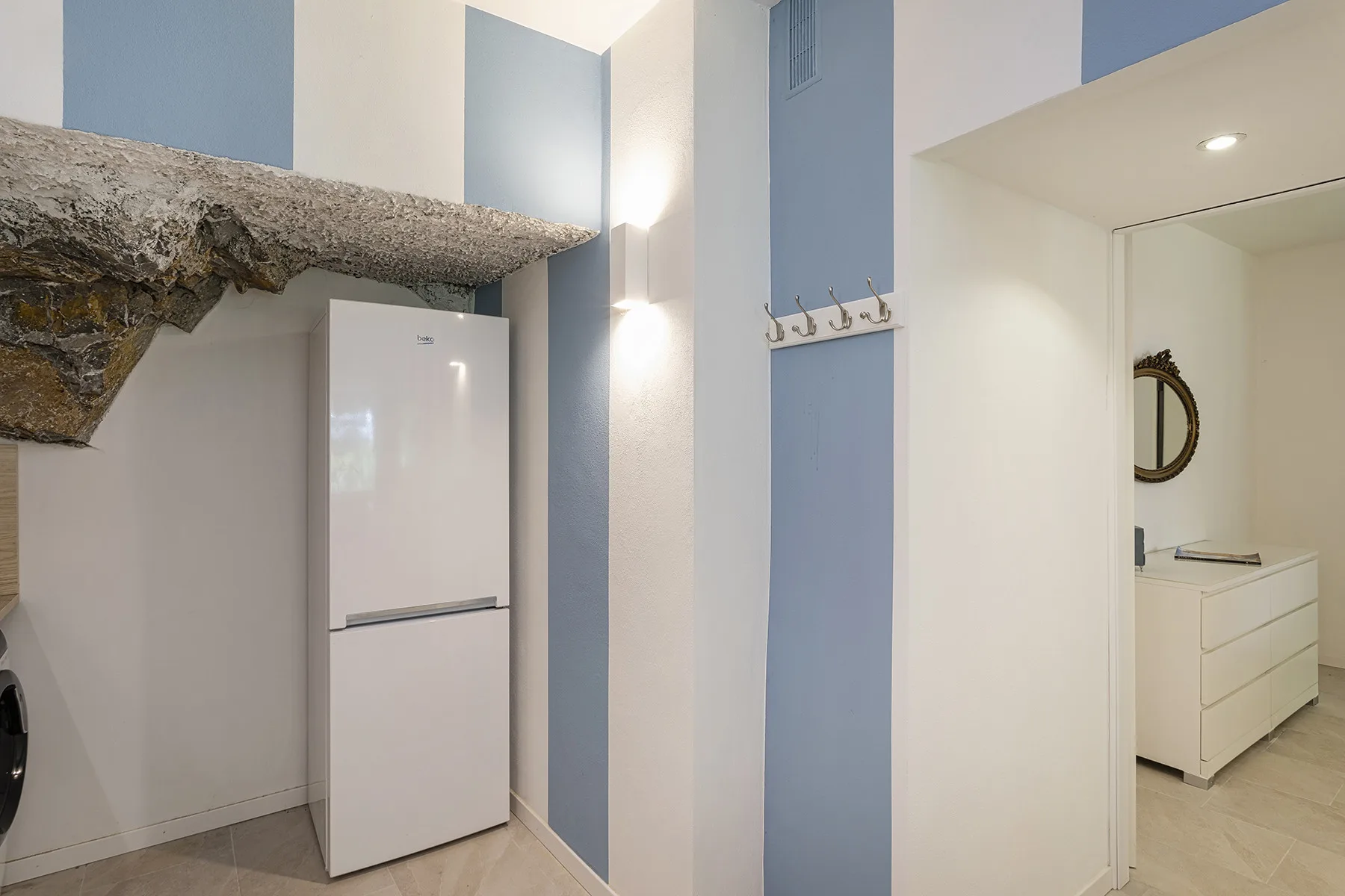 A bright interior hallway with a refrigerator and wall hooks beside a bathroom vanity.