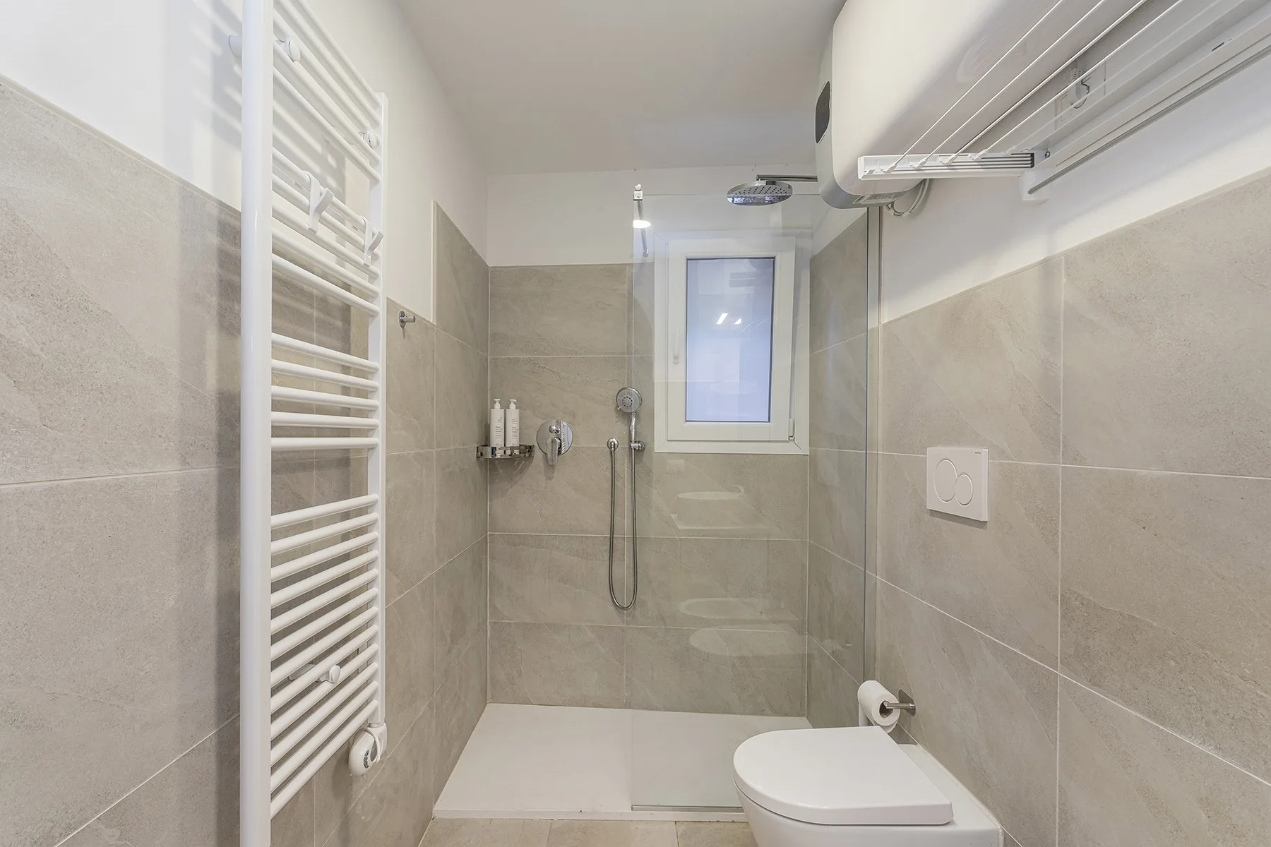 A tiled bathroom with a shower, small window, and wall-mounted towel radiator.