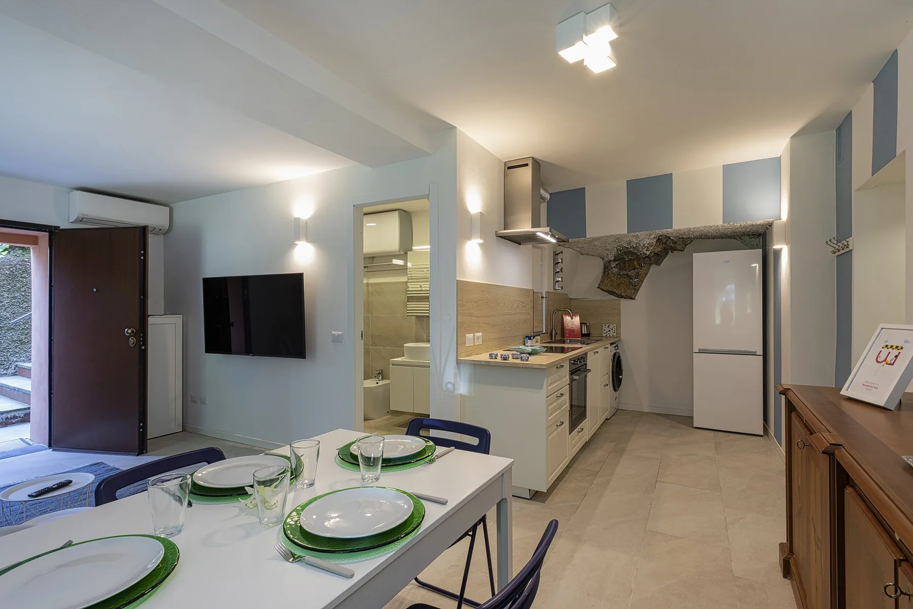 Un comedor y una cocina compacta comparten un espacio abierto, con una mesa preparada para comer.