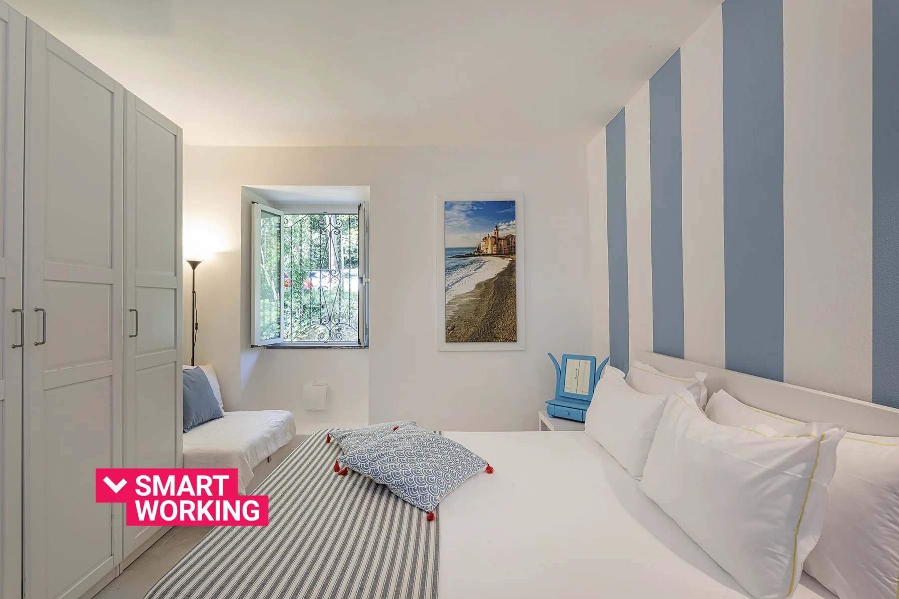 A bright bedroom with white bedding, striped wall accents, and a window overlooking greenery.