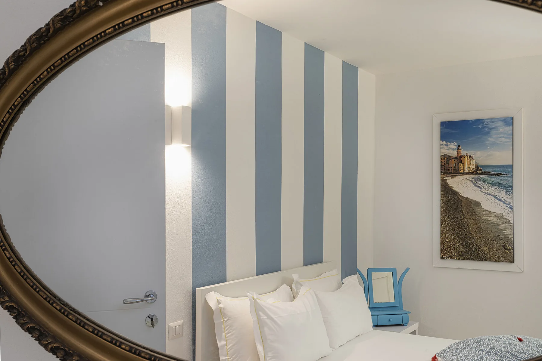 A bedroom with a bed, blue-and-white striped wall, and framed beach picture.