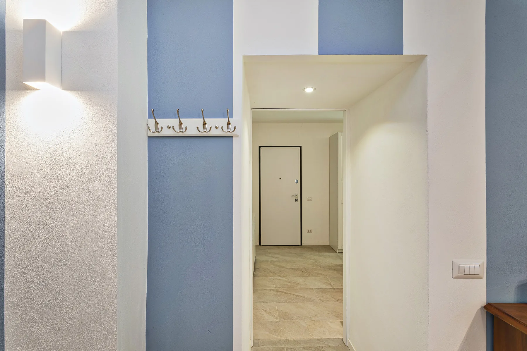 An interior hallway with a blue accent wall, coat hooks, and a doorway.