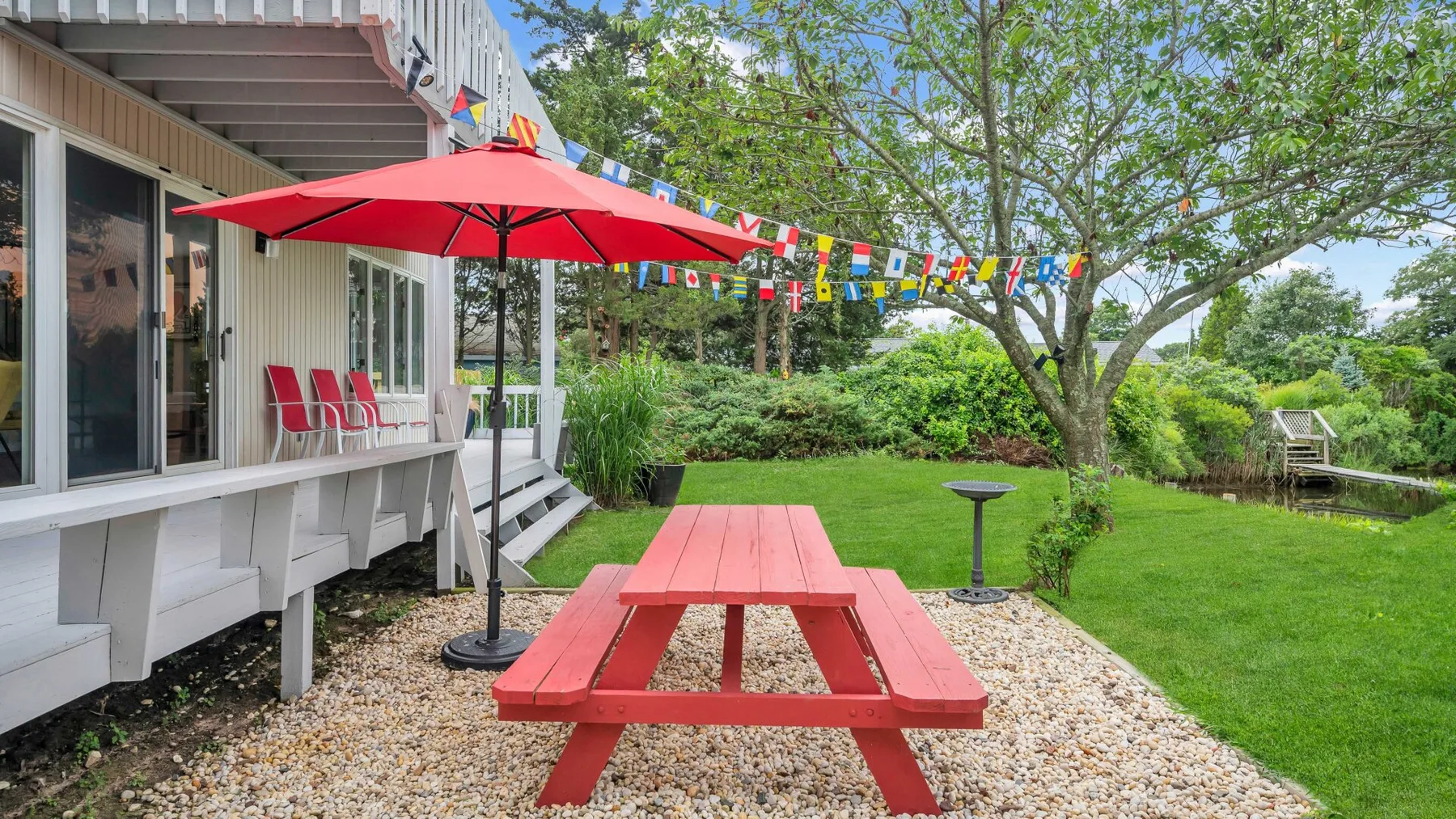 Zona de picnic al aire libre junto a una terraza, con sombrilla roja y vegetación.