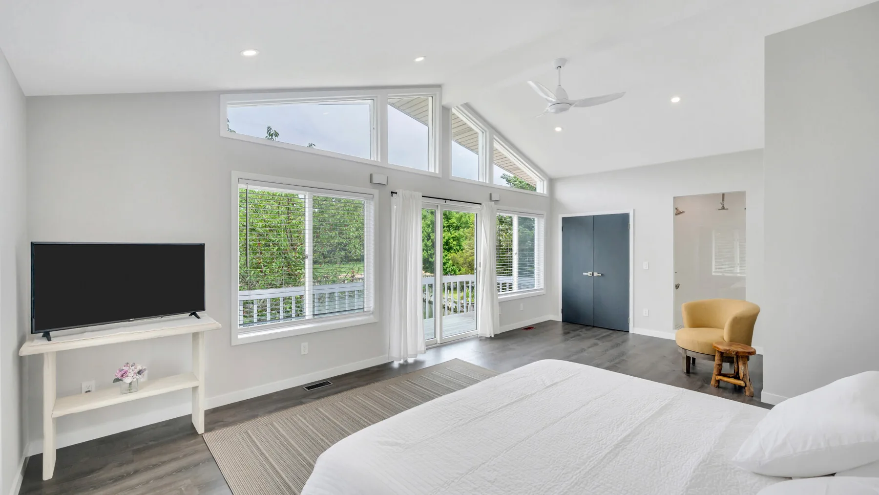 Un dormitorio luminoso con una cama, grandes ventanas y una zona de descanso.