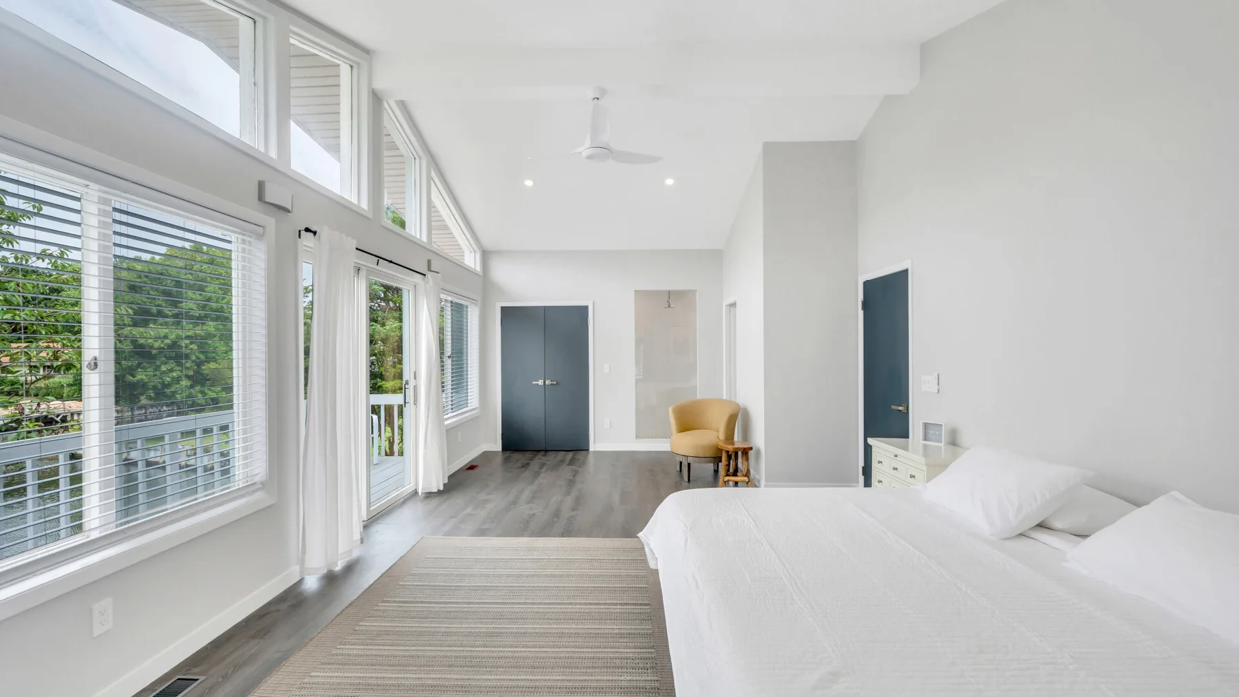 Un dormitorio luminoso con una cama grande junto a ventanas altas y una alfombra a rayas.