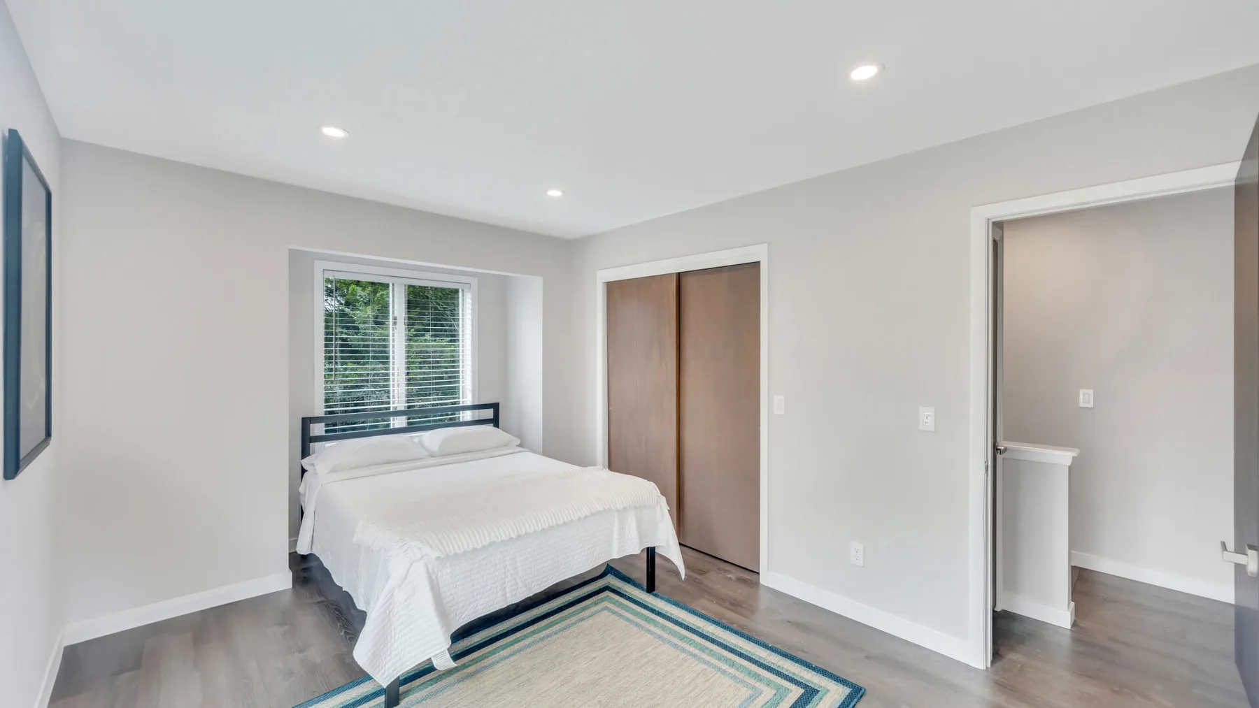 Un dormitorio luminoso con una cama, una ventana y puertas de armario de madera.