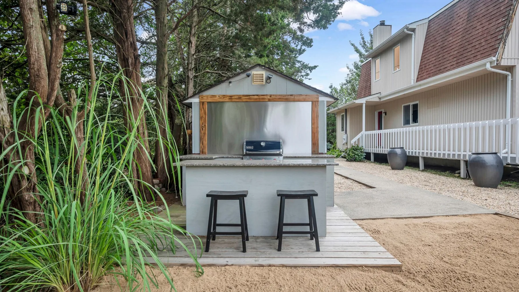 Una barra exterior con taburetes está junto a una casa y un jardín.