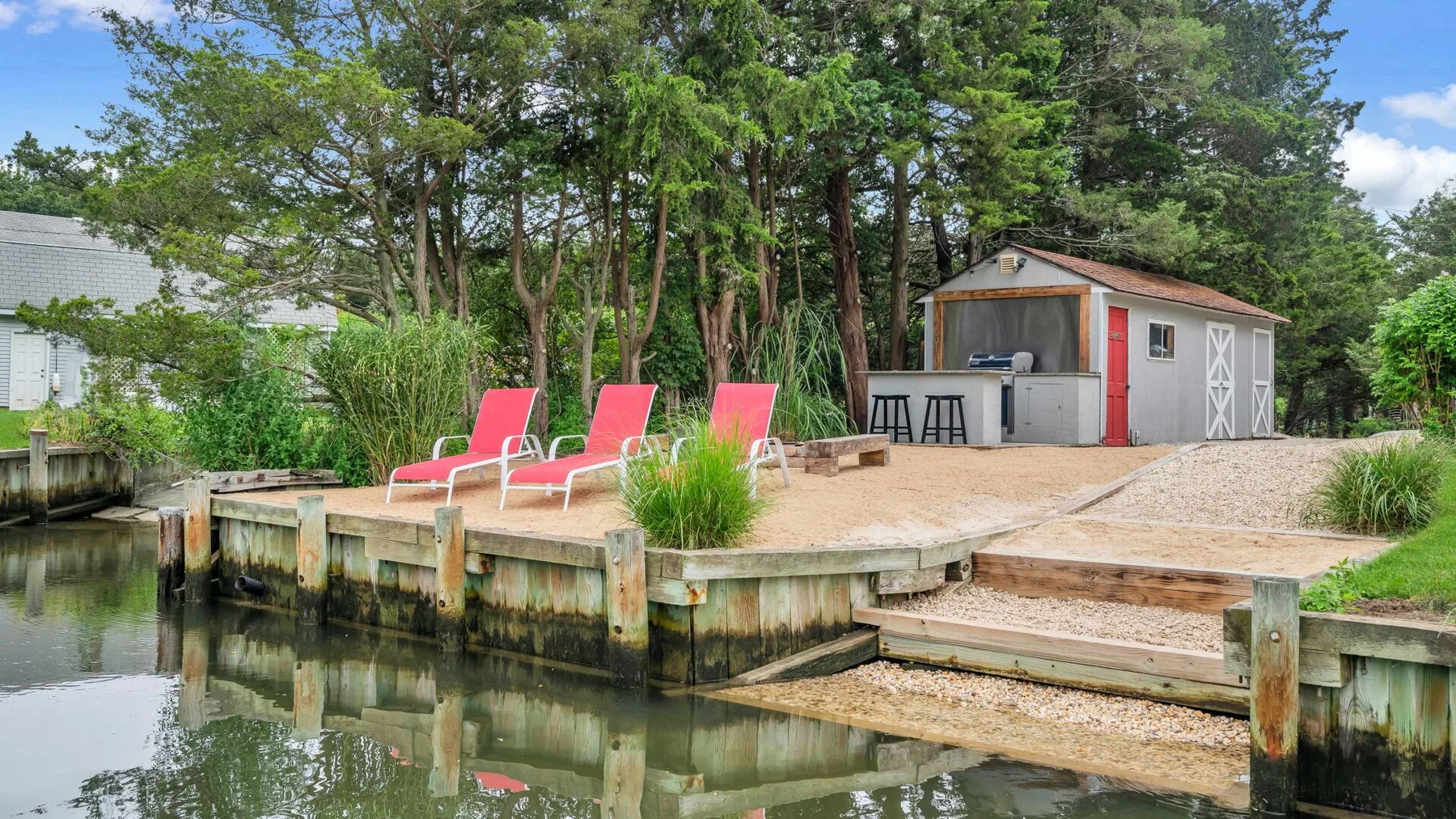 Una plataforma de madera junto al agua tiene asientos reclinables y un pequeño cobertizo.