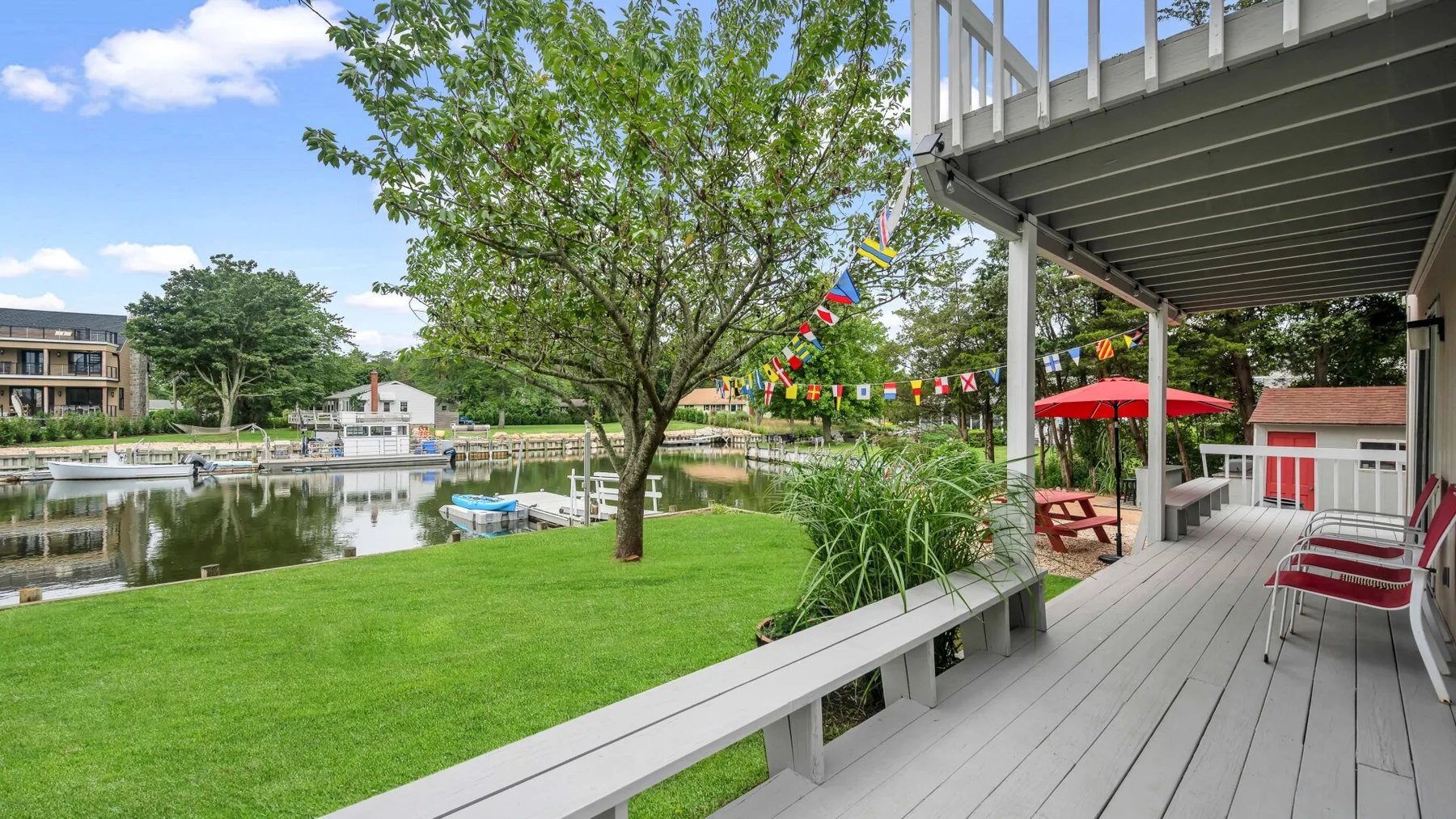 Un patio junto al lago da a un césped y un pequeño muelle, con asientos al aire libre bajo una terraza.