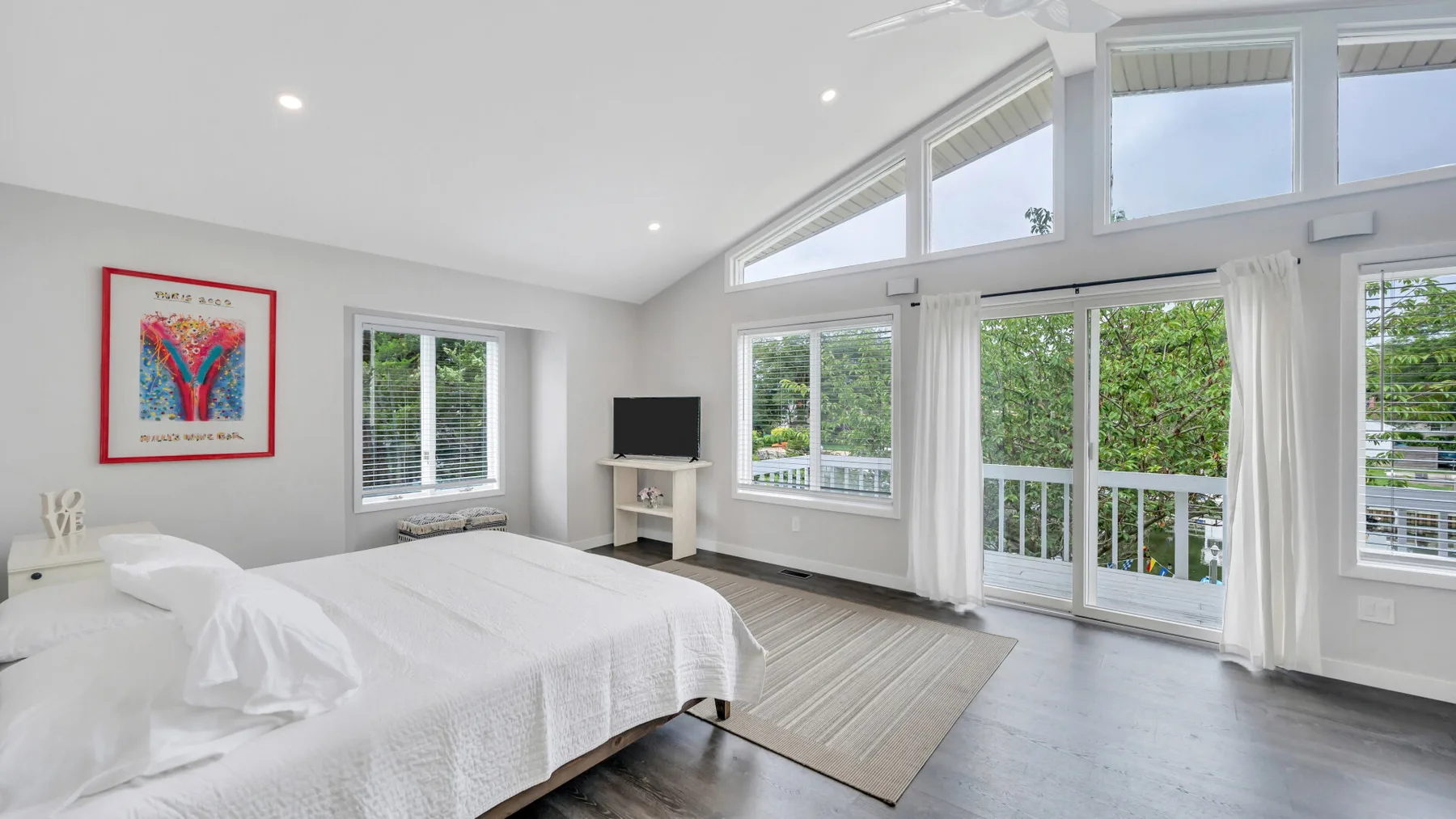 Un dormitorio luminoso con ropa de cama blanca y grandes ventanas con vistas a la vegetación.