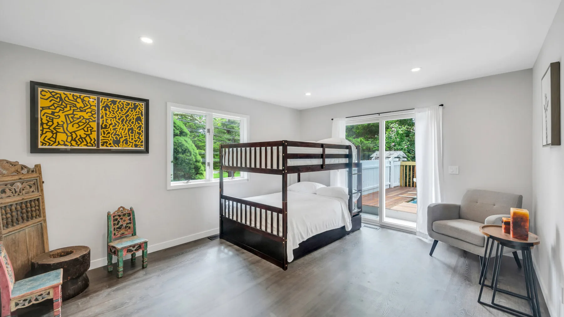 Un dormitorio luminoso con una litera de madera oscura y ventanas con vistas a la vegetación.