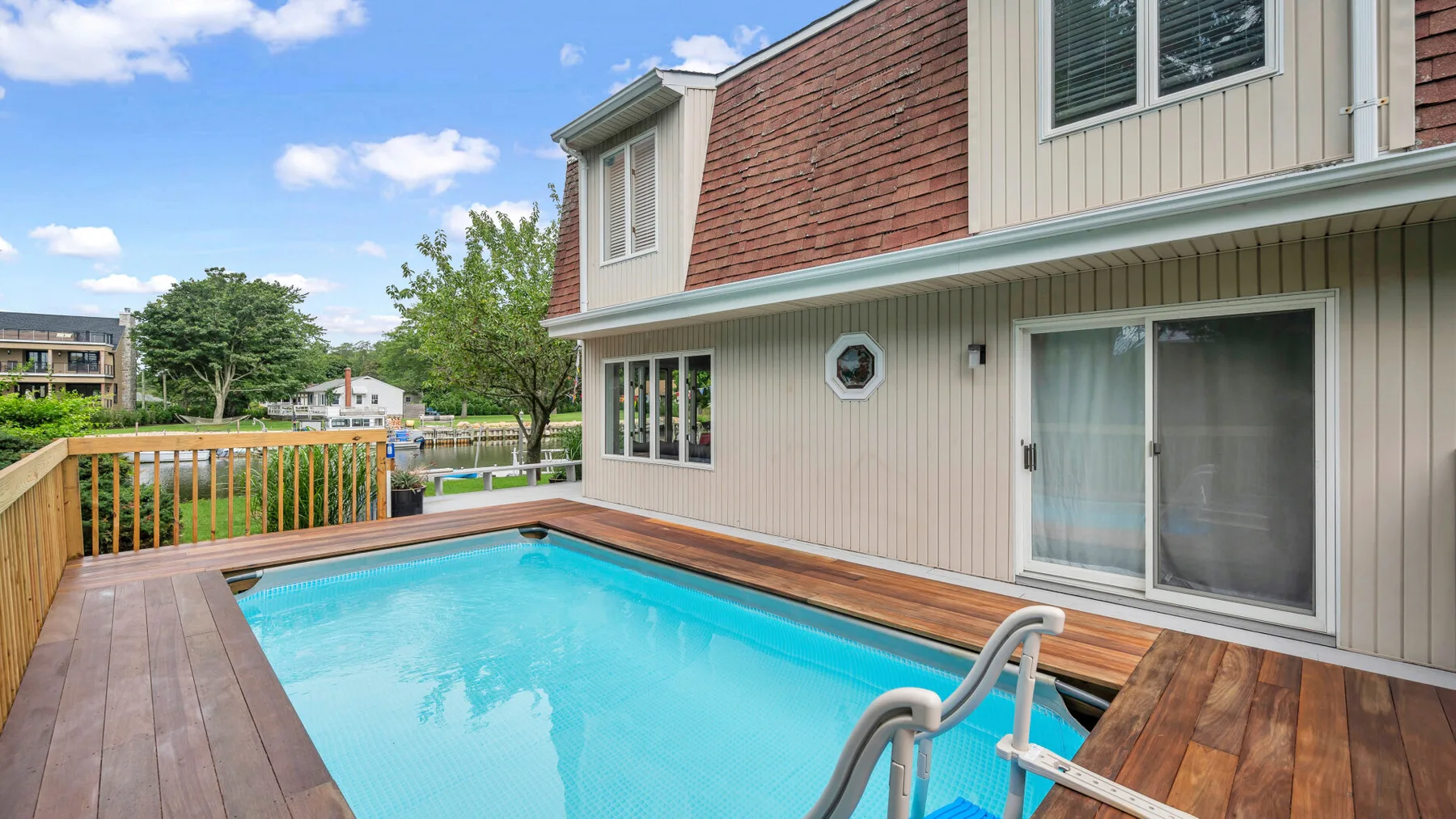Una piscina en el patio con una terraza de madera junto a una casa.