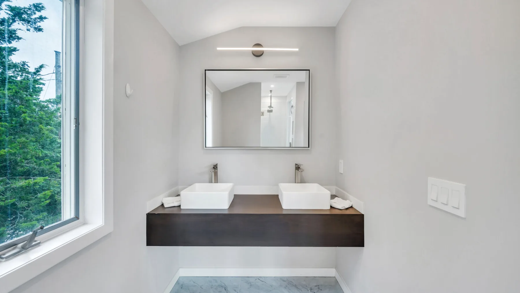 Un tocador de baño con dos lavabos está bajo un espejo junto a una ventana grande.
