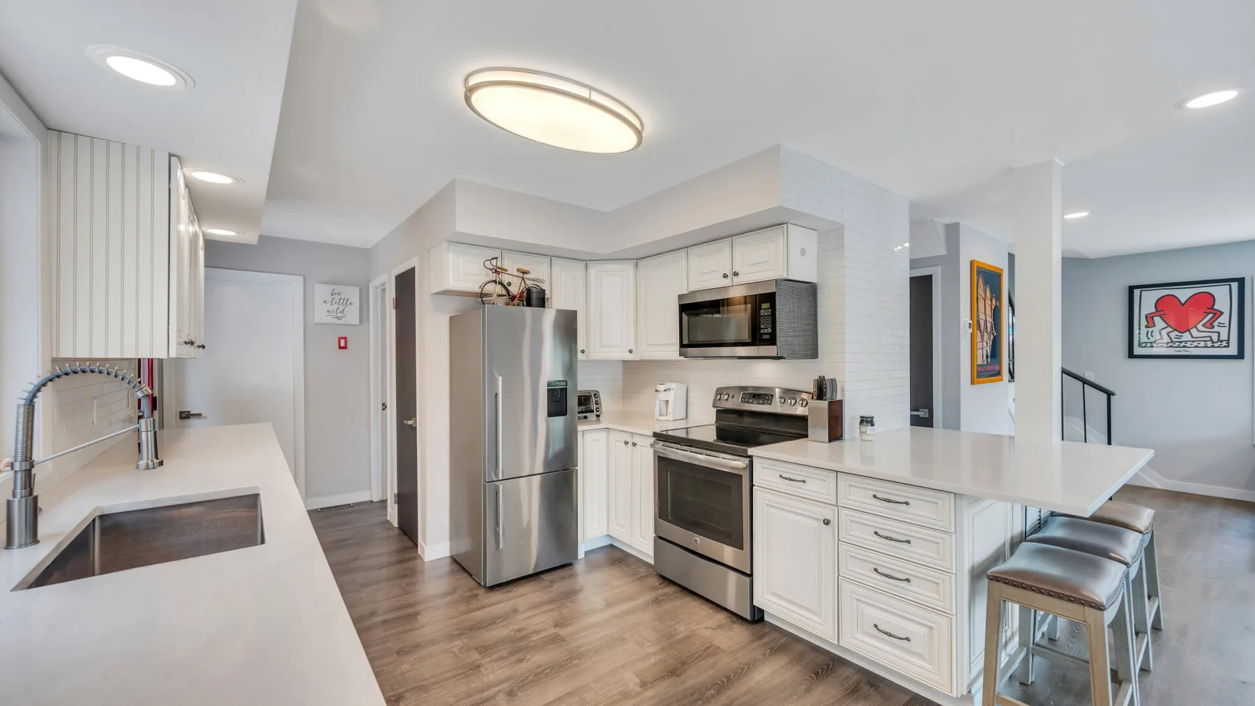 Una cocina moderna con gabinetes blancos, electrodomésticos de acero inoxidable y una barra.