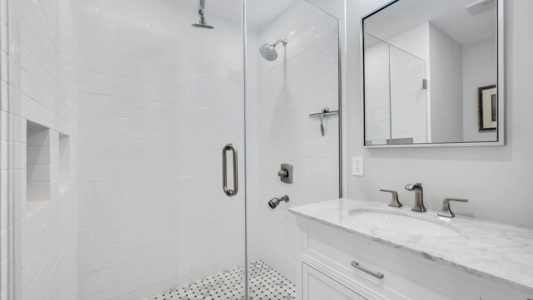 Un baño luminoso con una ducha de vidrio y un tocador blanco.