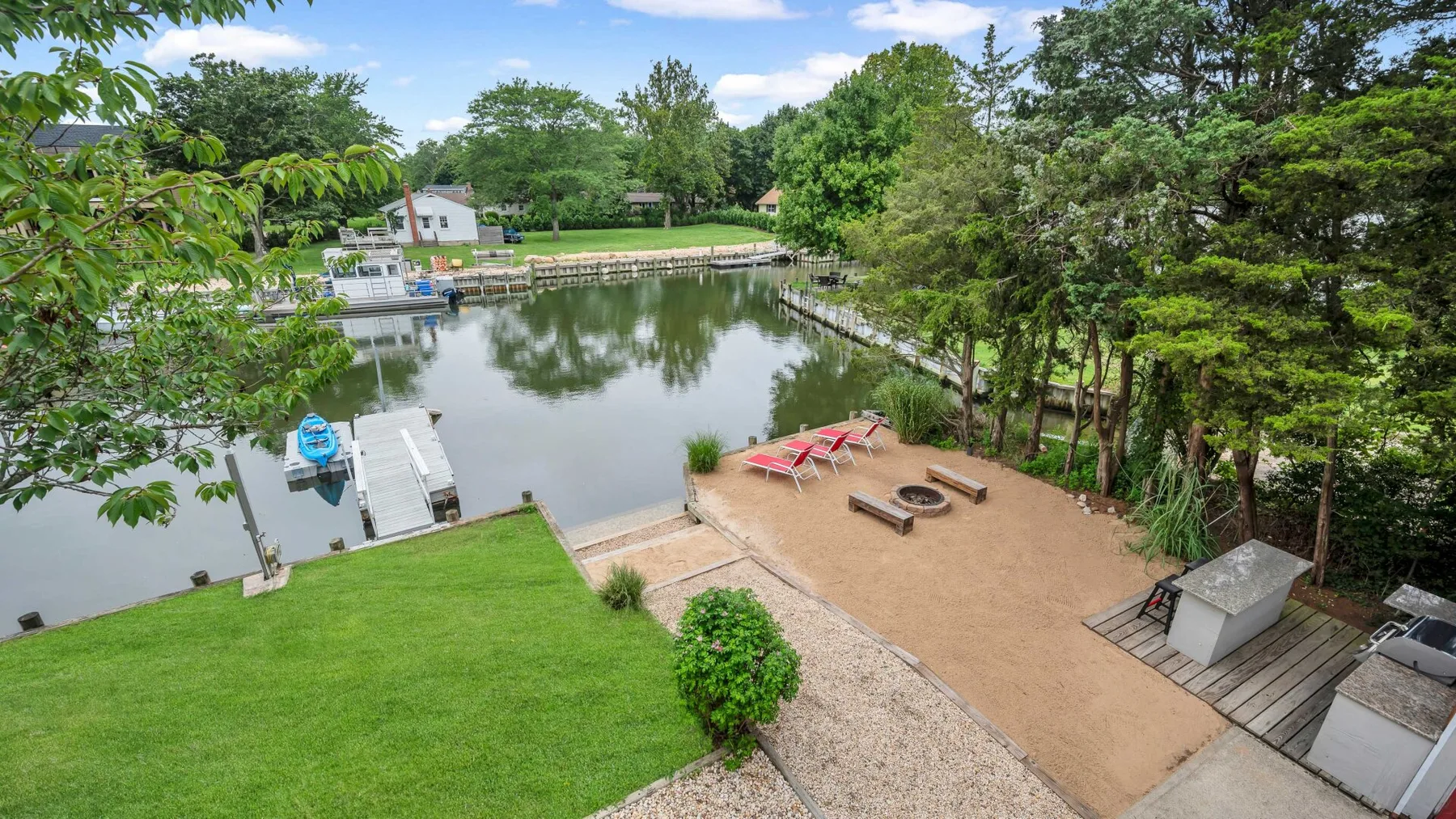 Un jardín junto al agua tiene un muelle, una zona de arena y asientos de picnic.