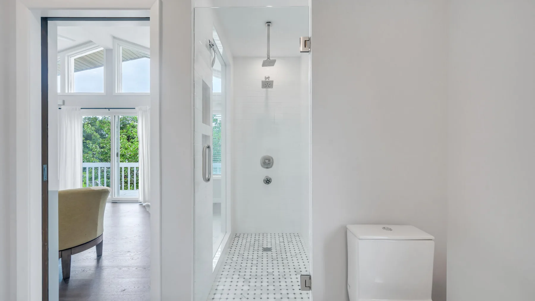 Un baño luminoso con una ducha de vidrio junto a una puerta abierta.