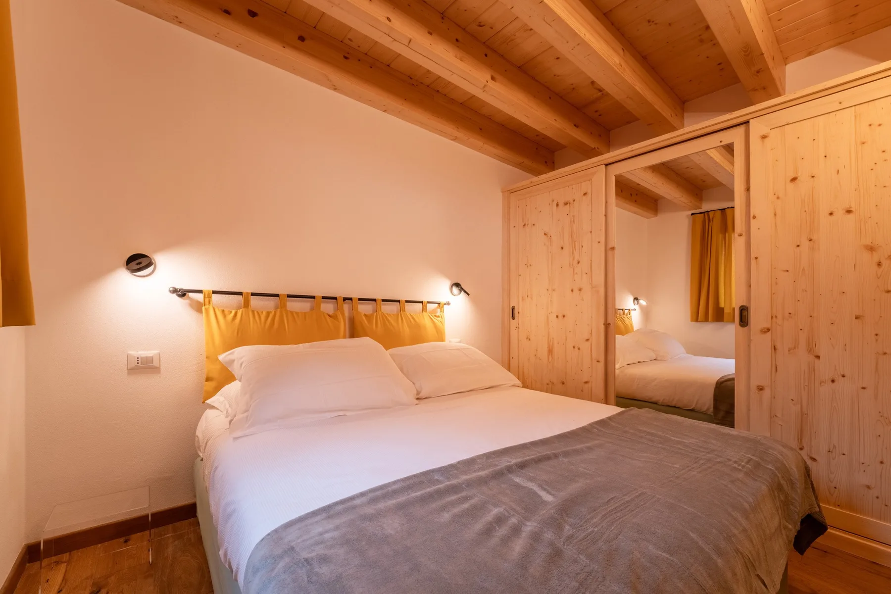 A bedroom with a bed, yellow curtains, and a mirrored wardrobe.