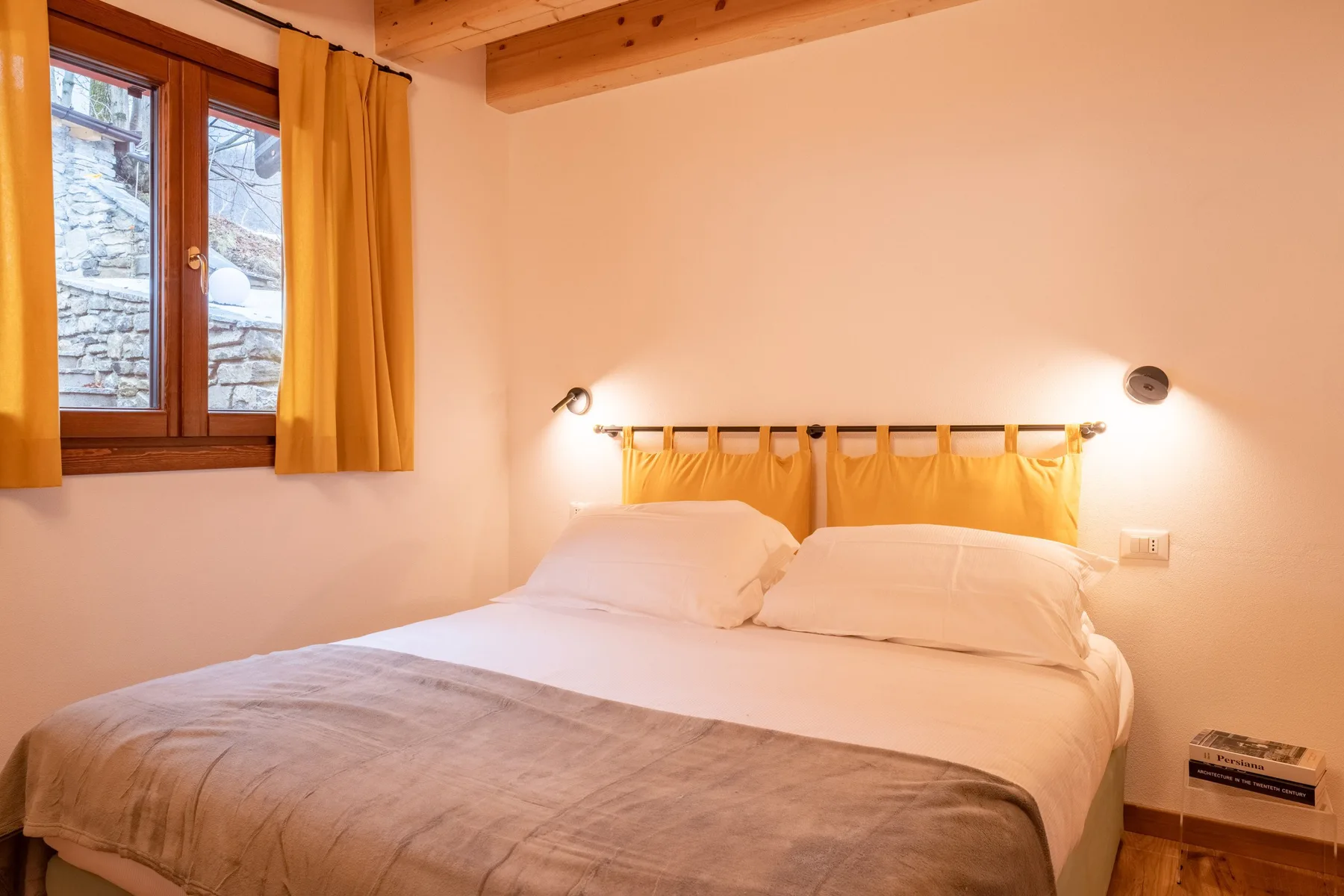 A bedroom with a bed beneath a wooden headboard and a curtained window.