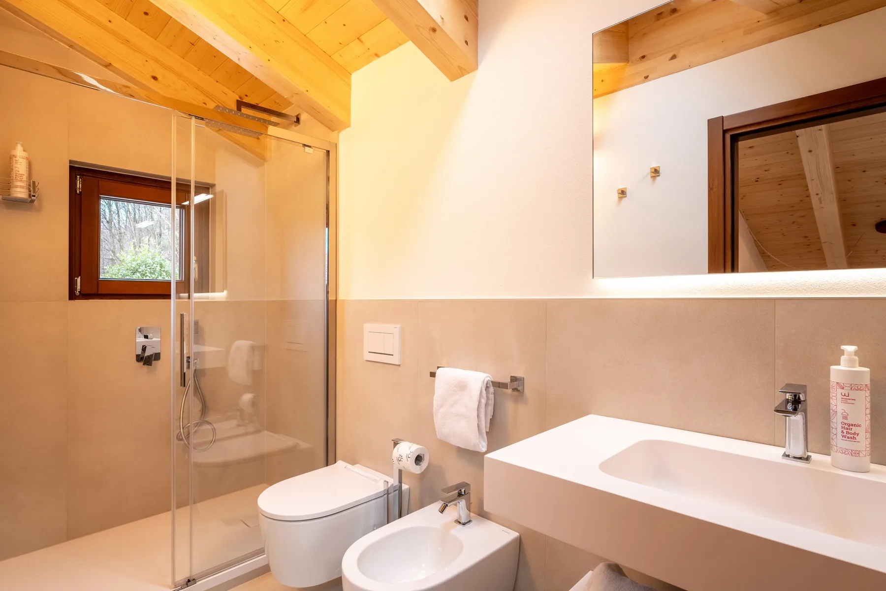 A bathroom with a glass shower, toilet, bidet, and wide sink counter.