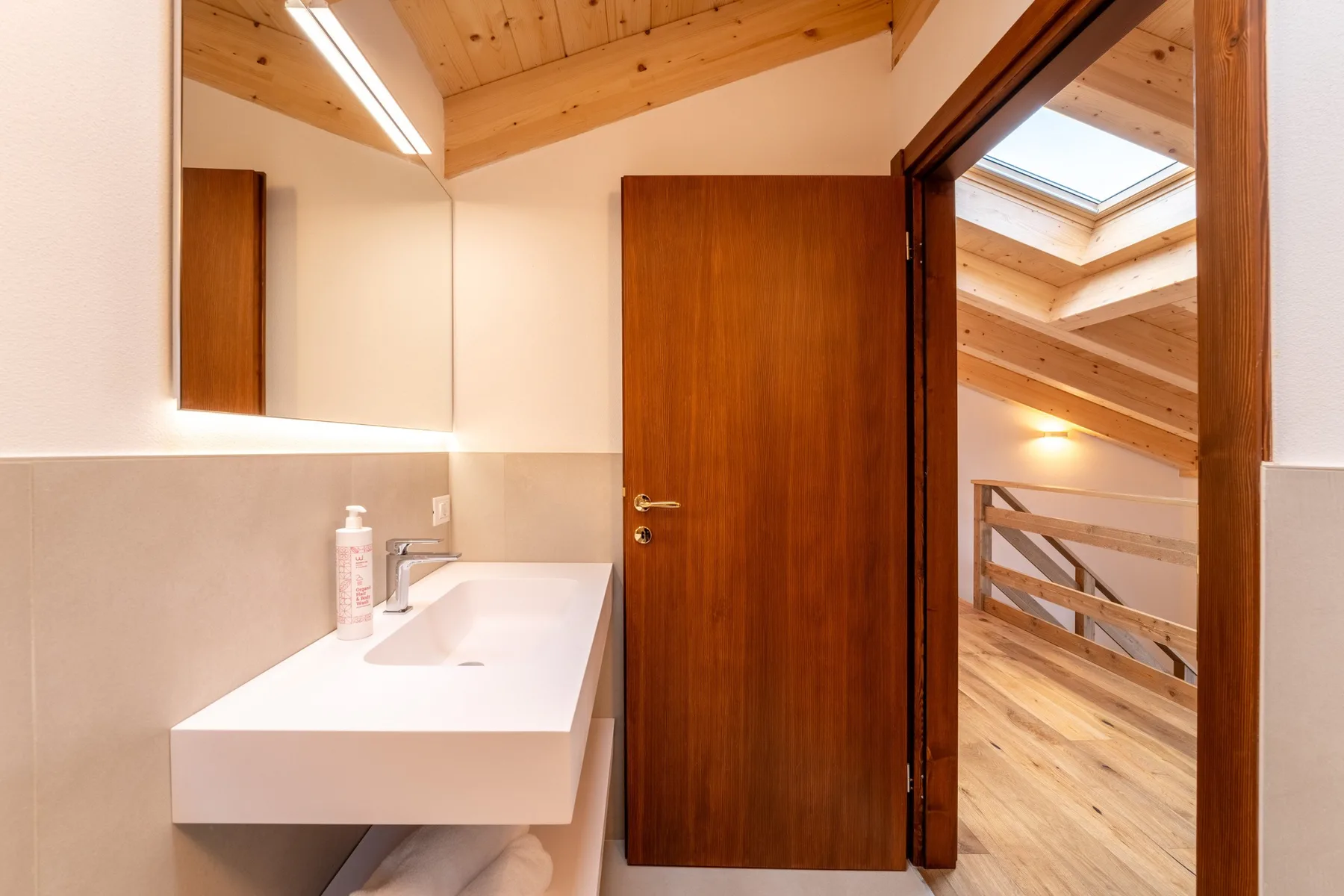 A bathroom vanity and sink sit beside an open doorway to a wood-floored interior.