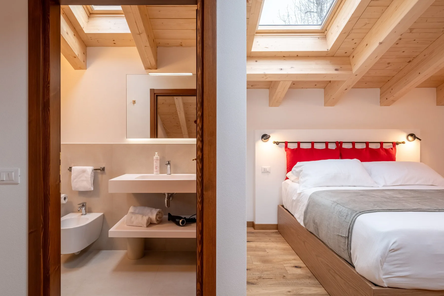 A bedroom with a large bed beside an open bathroom under skylights.