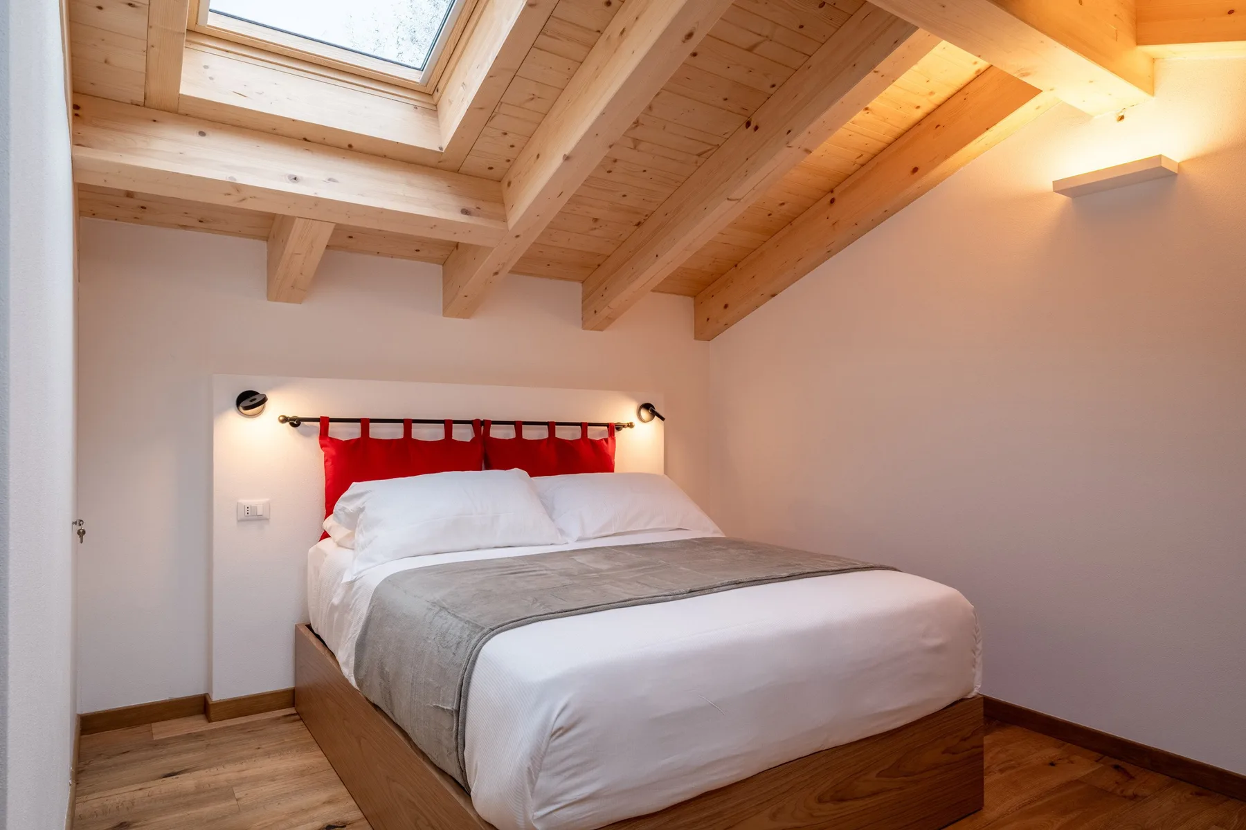 A bedroom with a bed beneath a wooden ceiling and skylight.