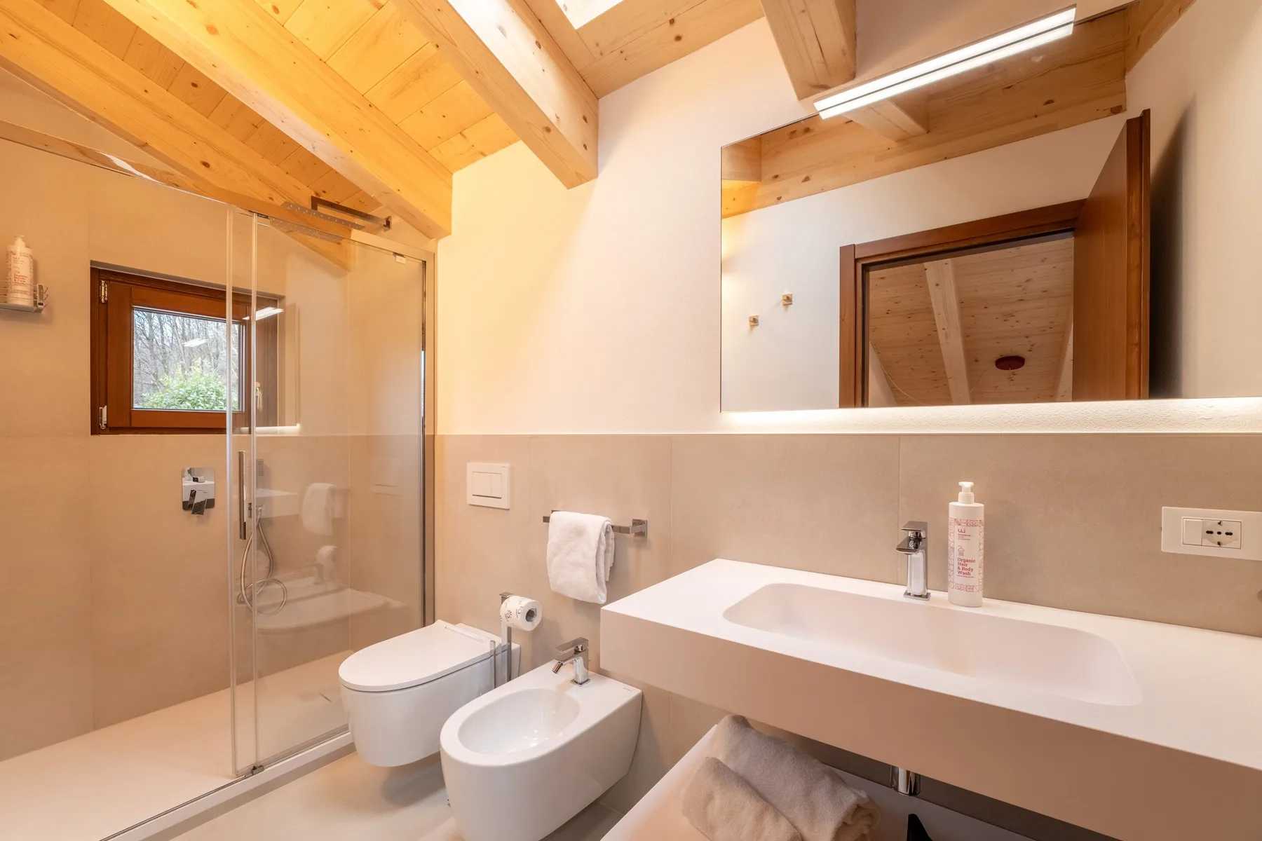 A bathroom with a glass shower, sink, and wood-paneled ceiling.