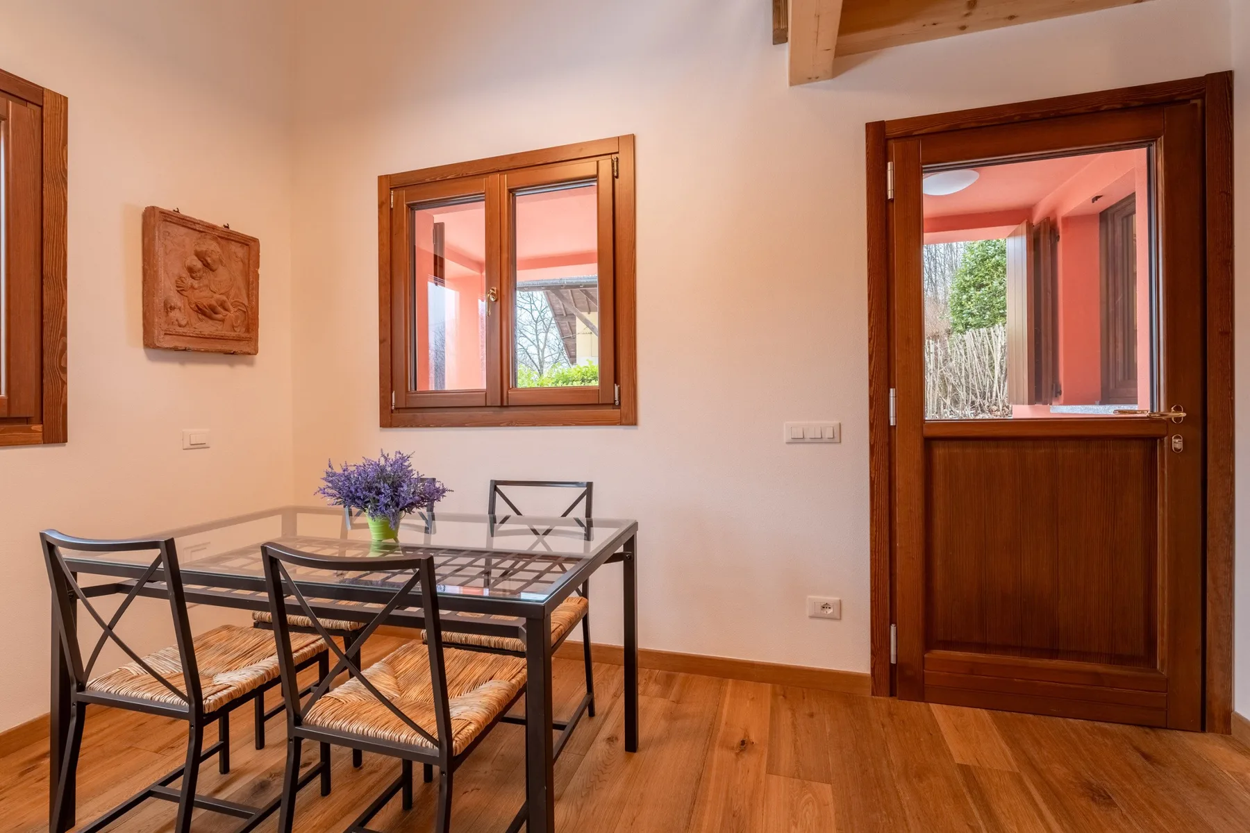 A dining area with a glass-top table and wooden chairs sits beside a window.