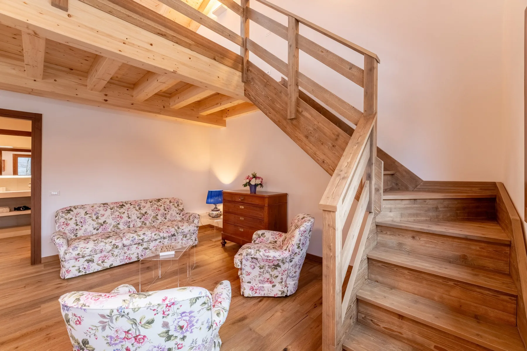 A living room with floral seating beneath a wooden staircase.
