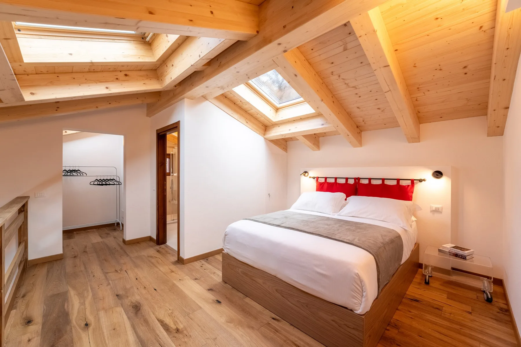 A bedroom with a bed beneath a sloped wooden ceiling and skylights.