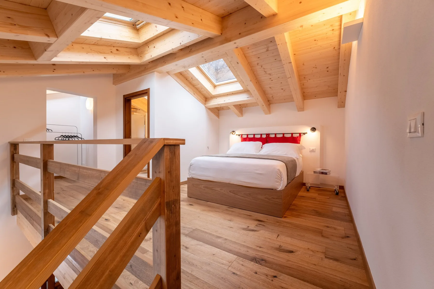 A bedroom beneath a sloped timber ceiling, with a bed and skylight.