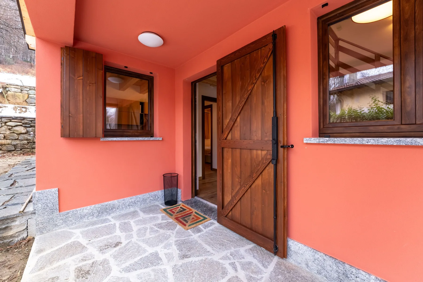 A coral-colored entryway with an open wooden door and stone paving.