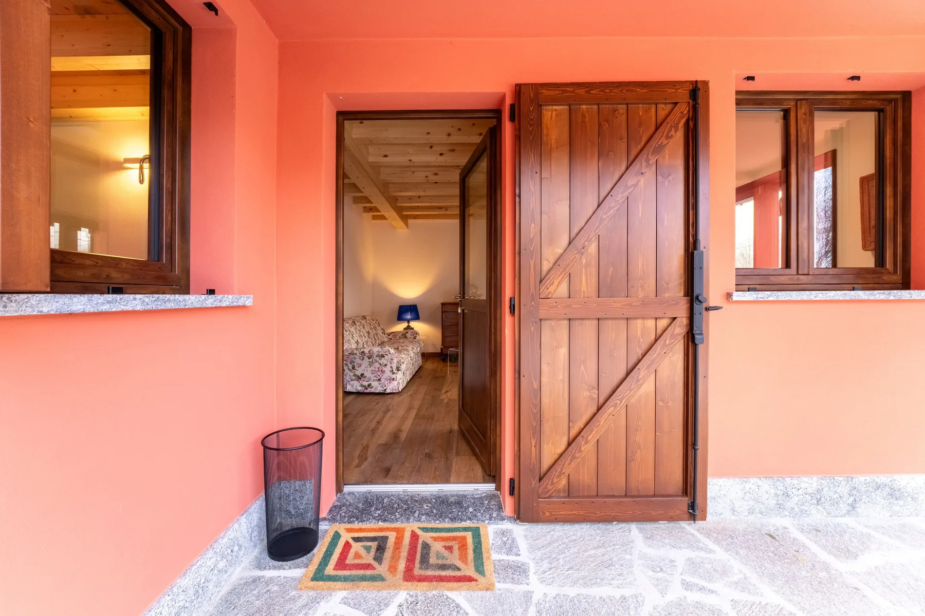 A pink exterior wall surrounds an open wooden doorway with a small patterned mat.